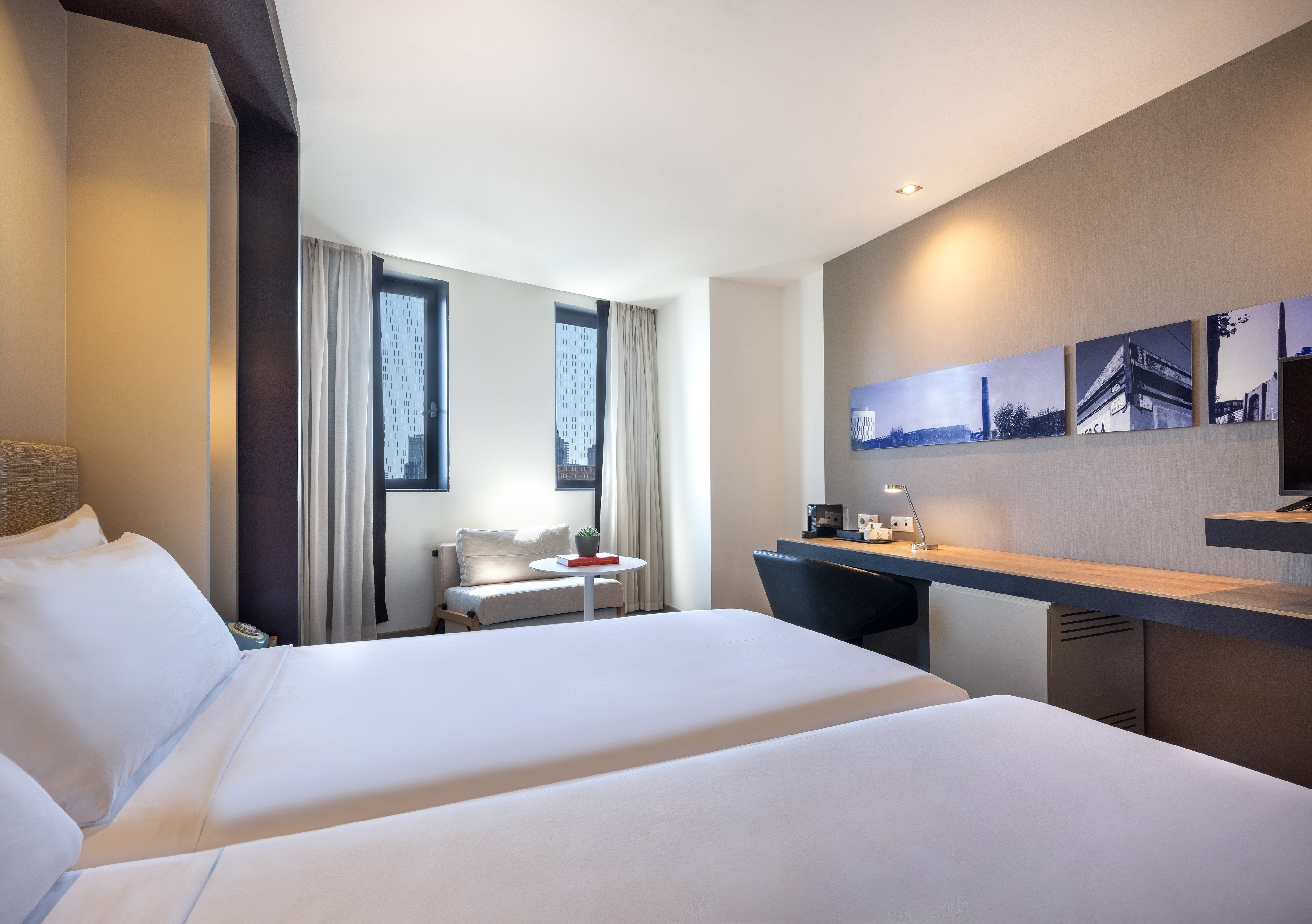 Hotel room with twin beds, modern desk area, and city view windows.