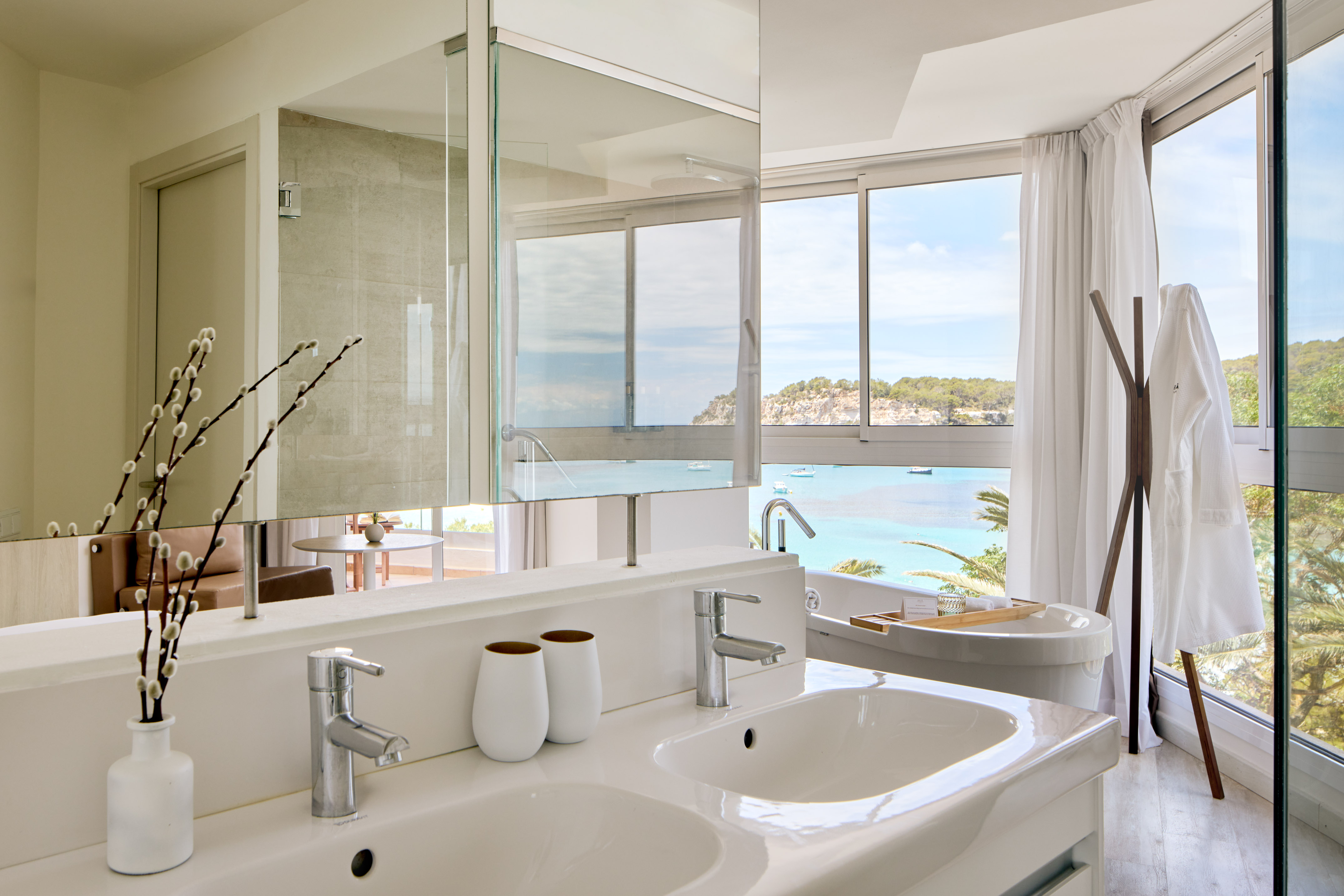 Modern bathroom with double vanity, bathtub, and panoramic ocean view.