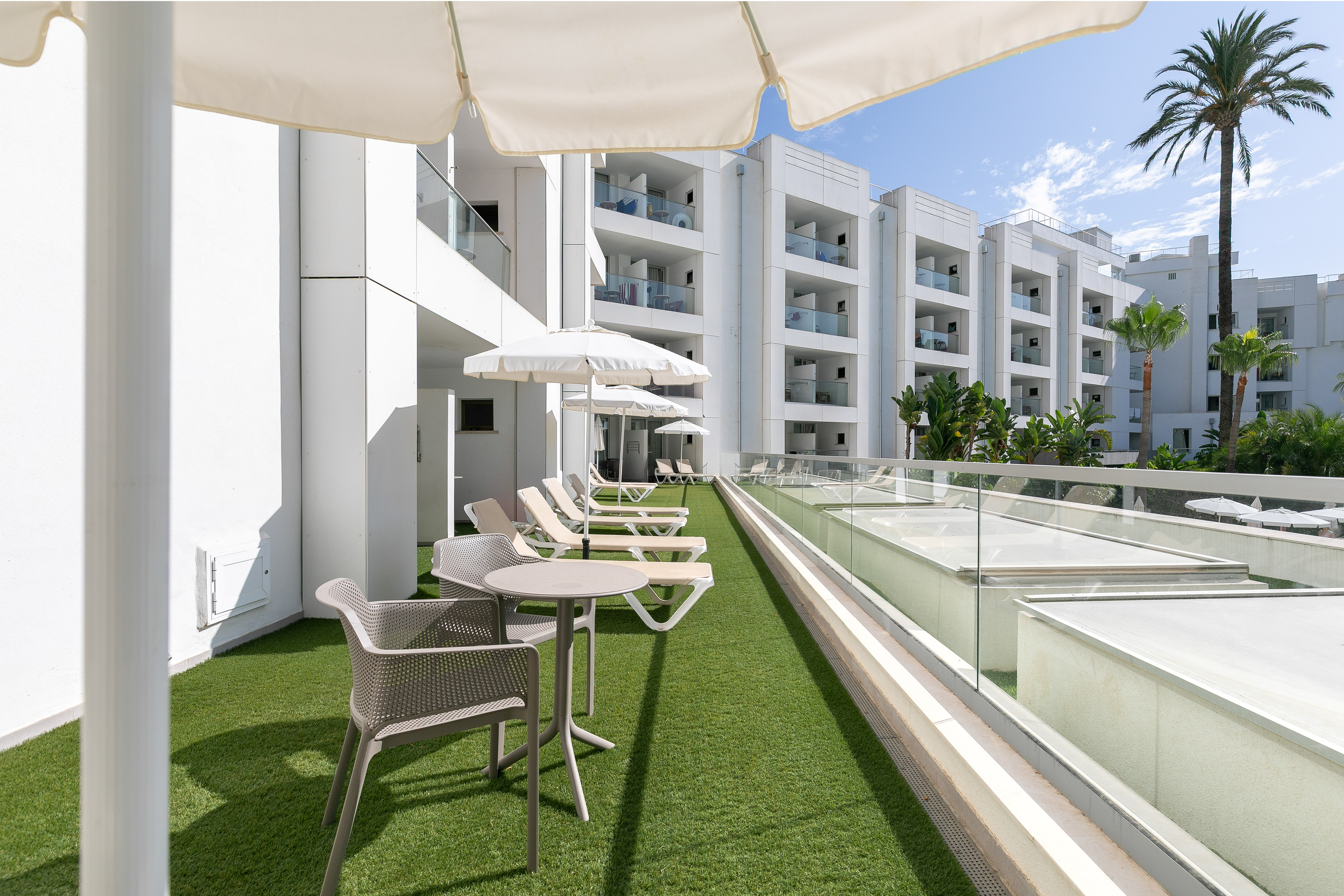 Sunny hotel rooftop terrace, artificial grass, sun loungers, white umbrellas.