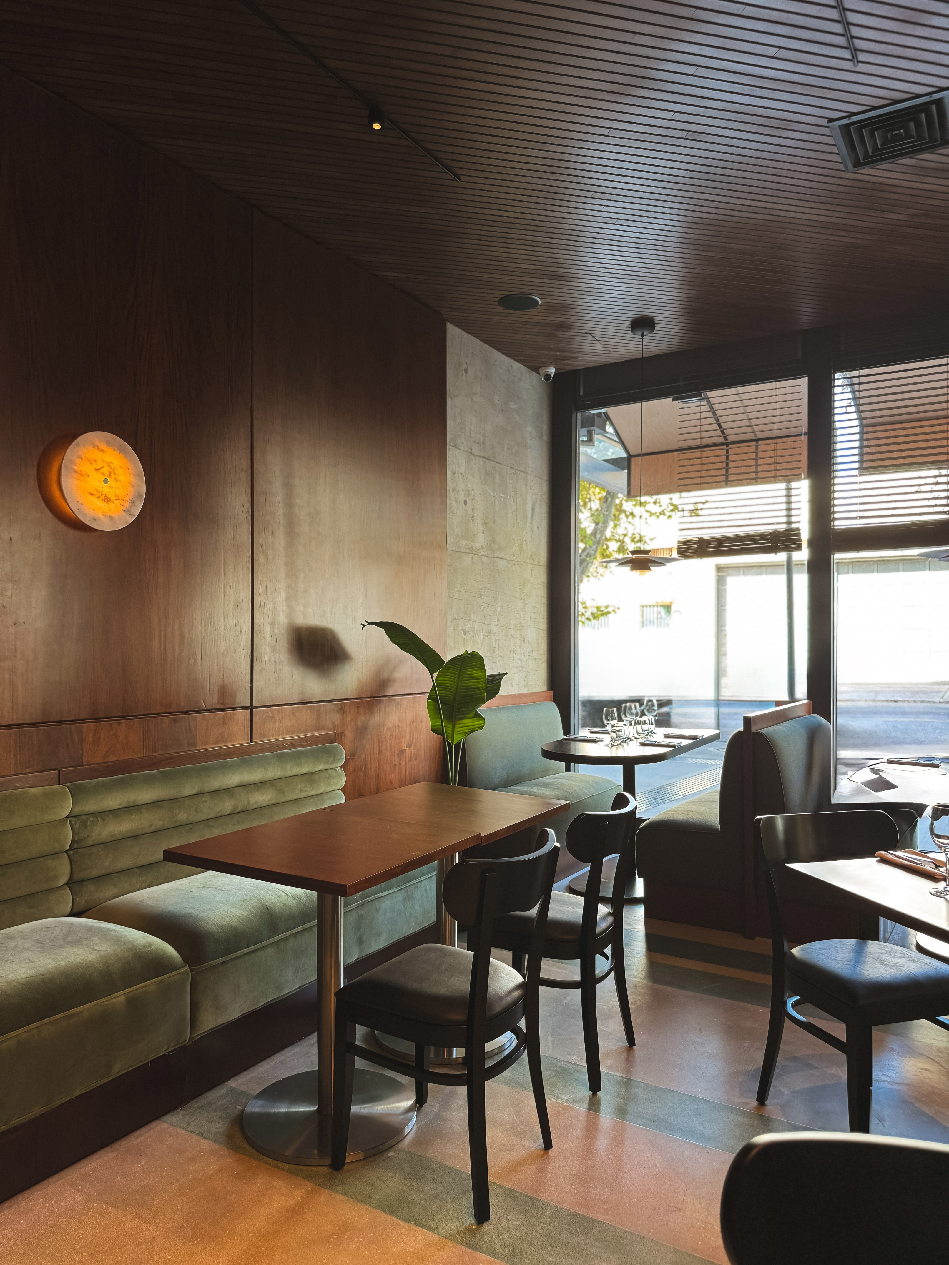 Restaurant interior with green velvet booths, dark wood walls, and modern tables.
