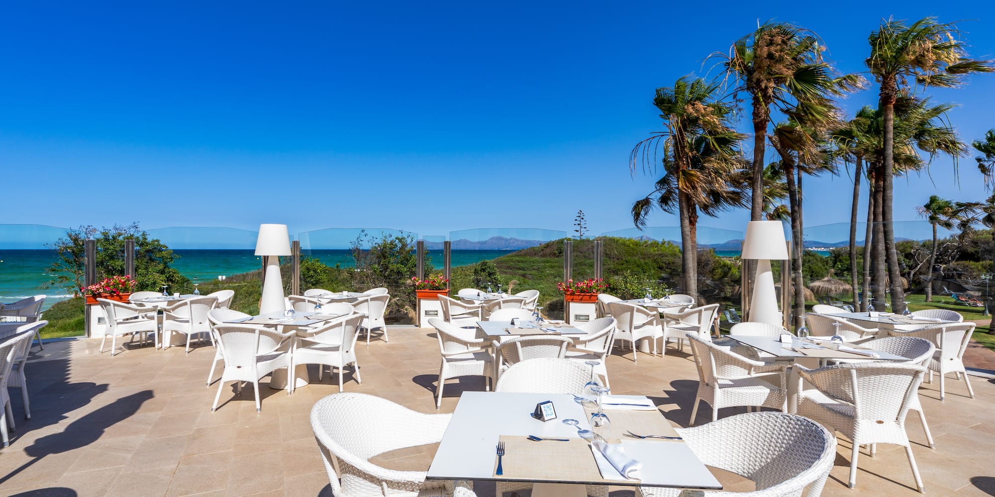 a white tables and chairs on a patio with a body of water in the background