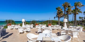 a white tables and chairs on a patio with a body of water in the background