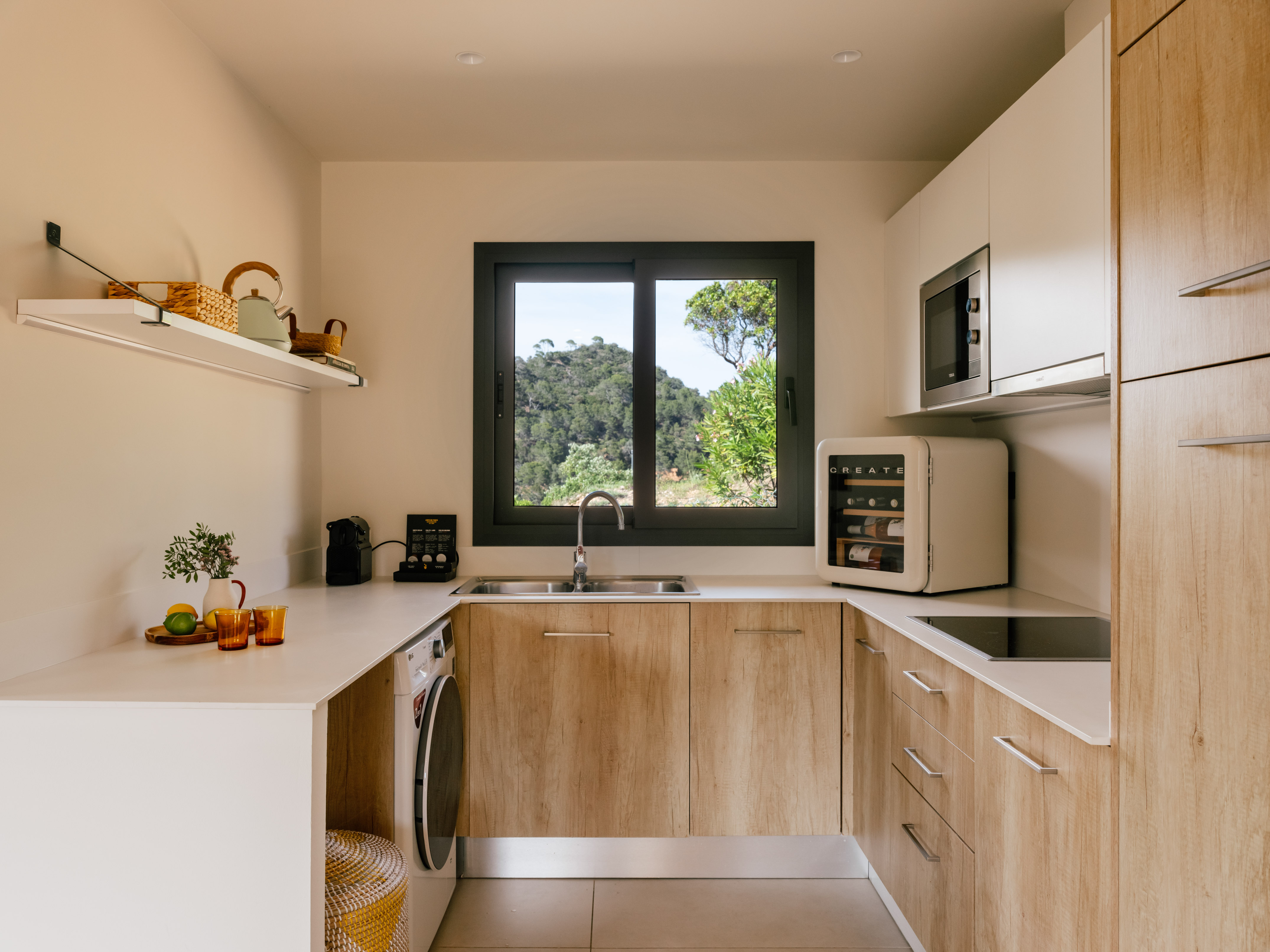 U-shaped modern kitchen with wood cabinets, white countertops, and nature view.