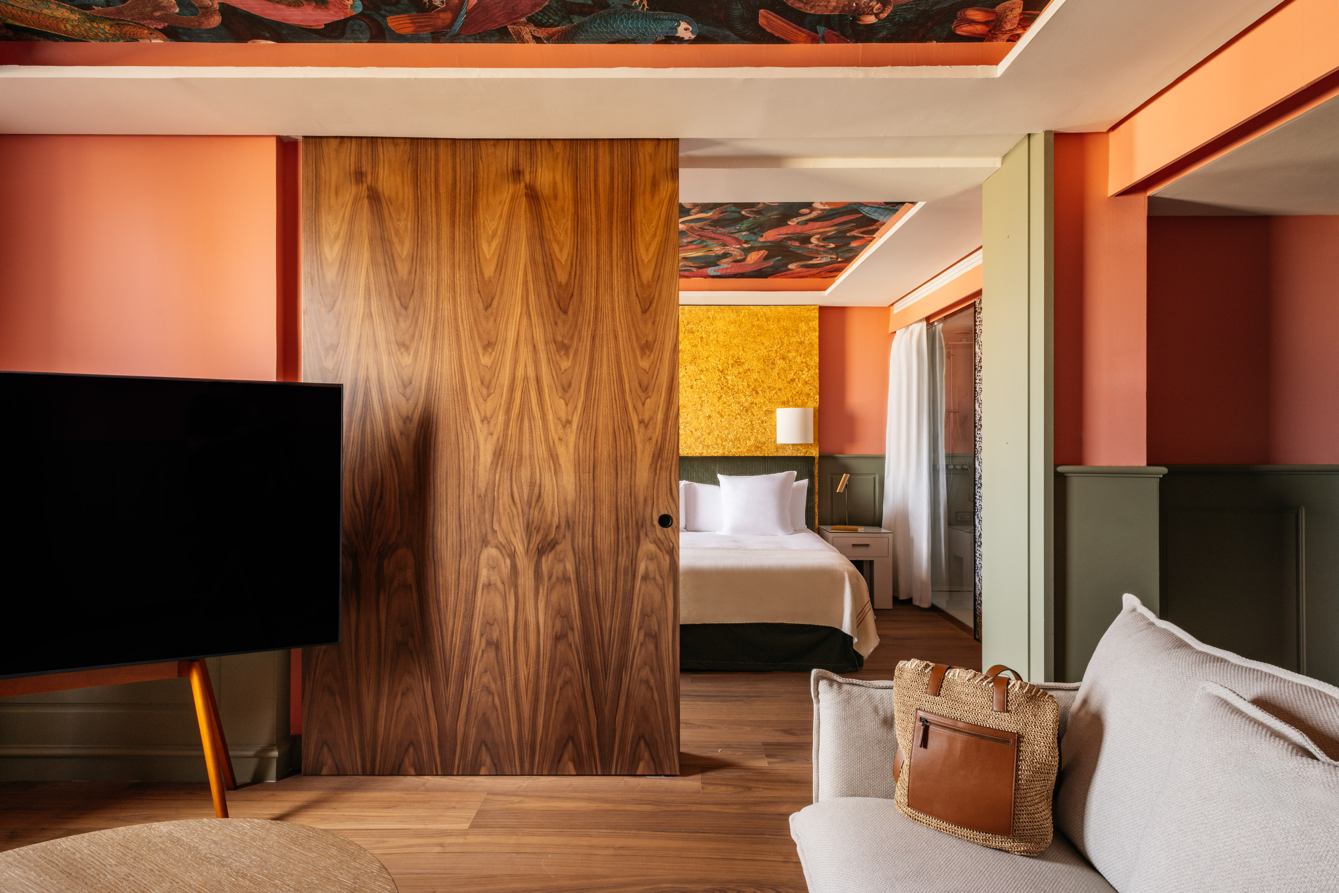 Stylish hotel suite: coral walls, wood sliding door to bedroom, and ornate ceiling.
