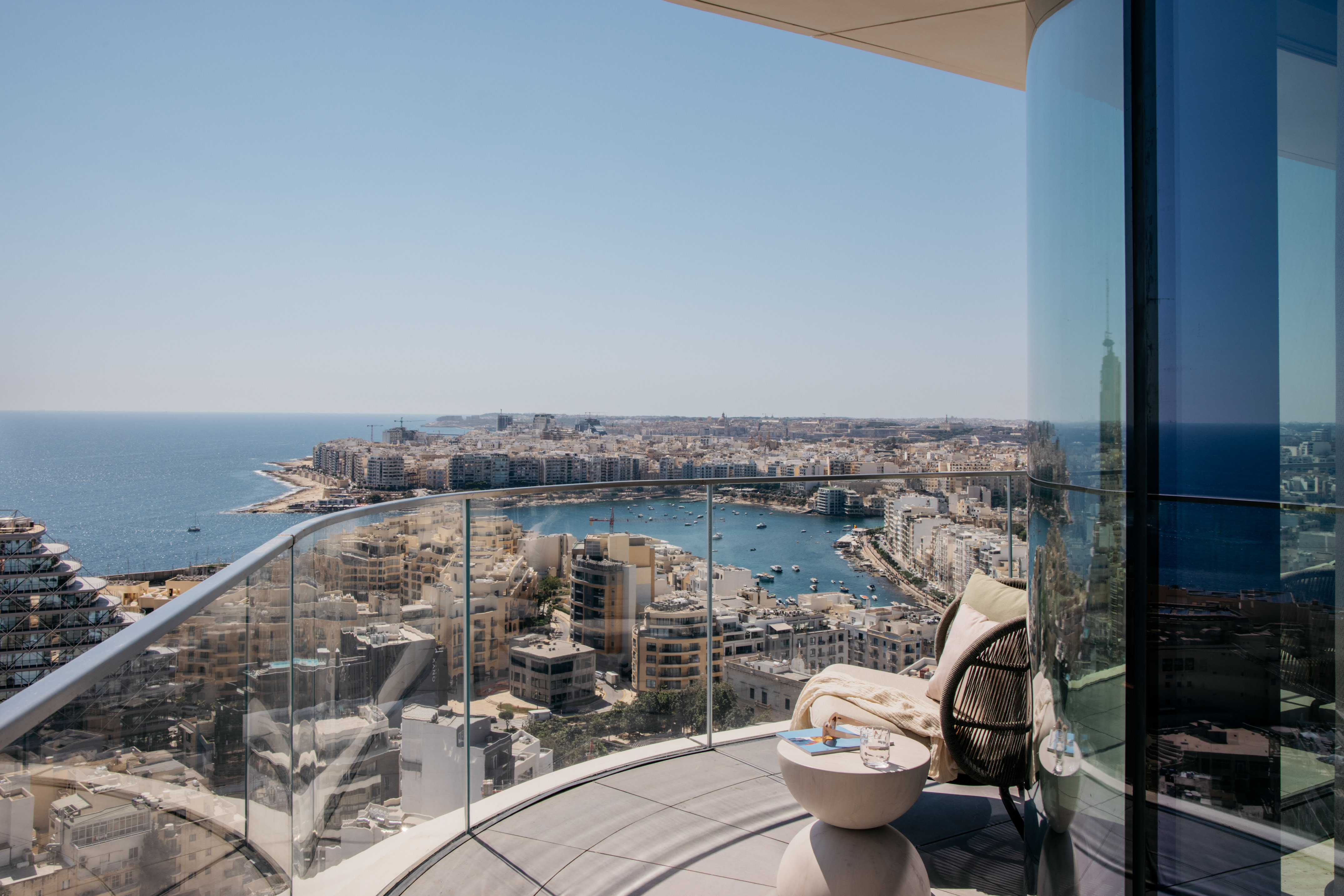 Panoramic balcony view of a sunny Mediterranean city, harbor, and sea.