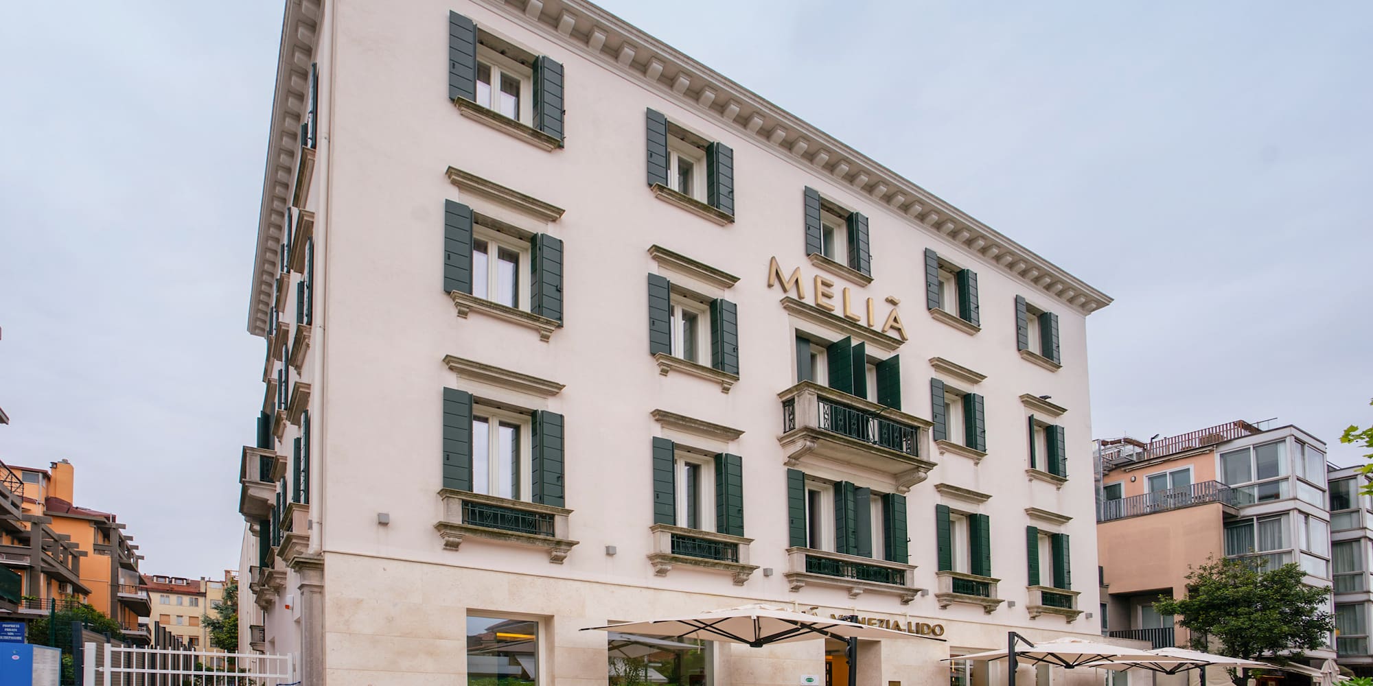 Melia Venezia Lido hotel exterior with green shutters and outdoor cafe seating.