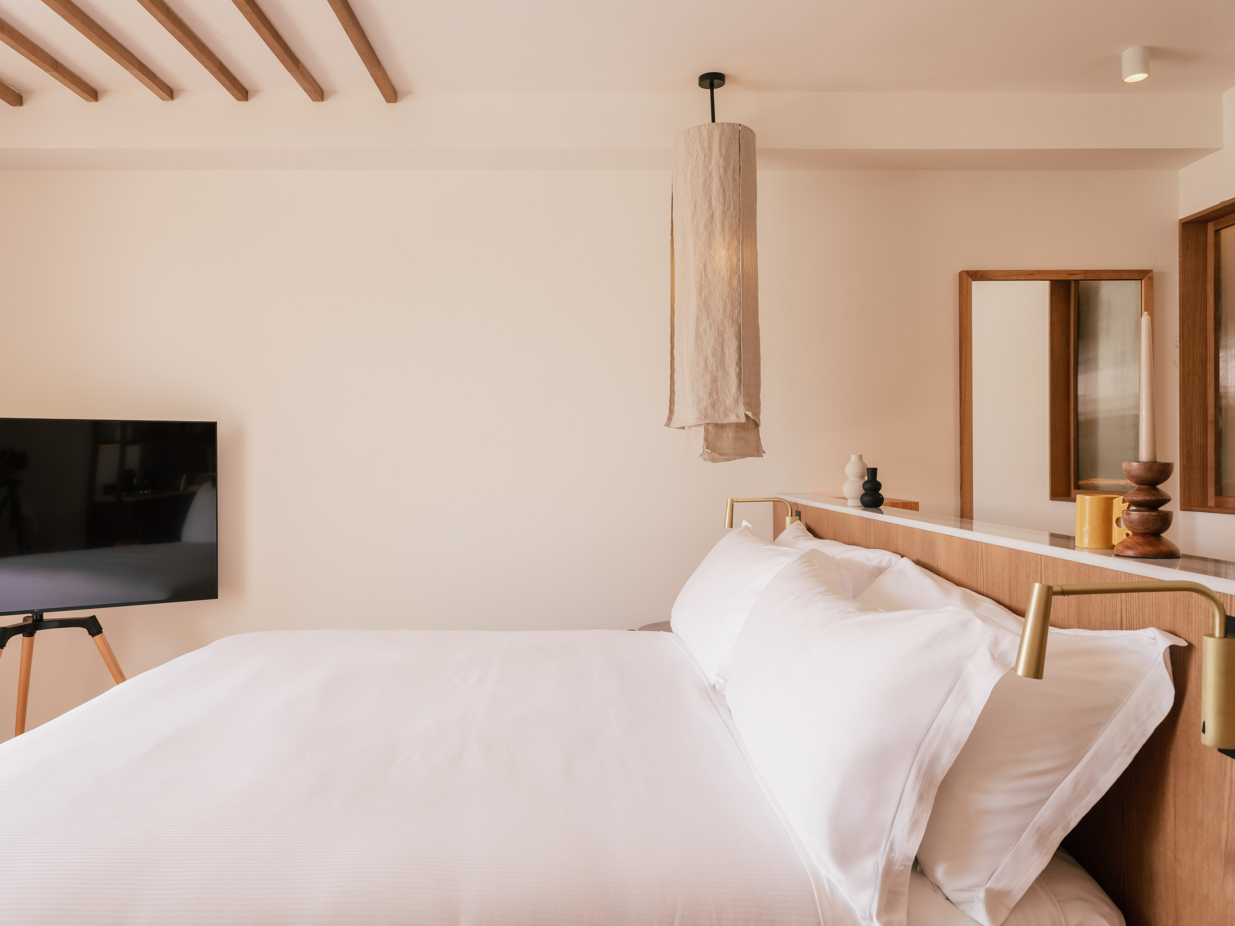 Modern hotel room with white bed, wooden headboard, and fabric pendant light.