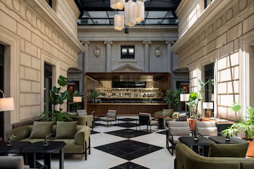 Elegant hotel lobby bar with checkered floor, green sofas, and glass skylight.
