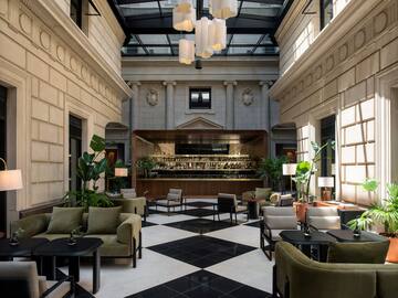 Elegant hotel lobby bar with checkered floor, green sofas, and glass skylight.