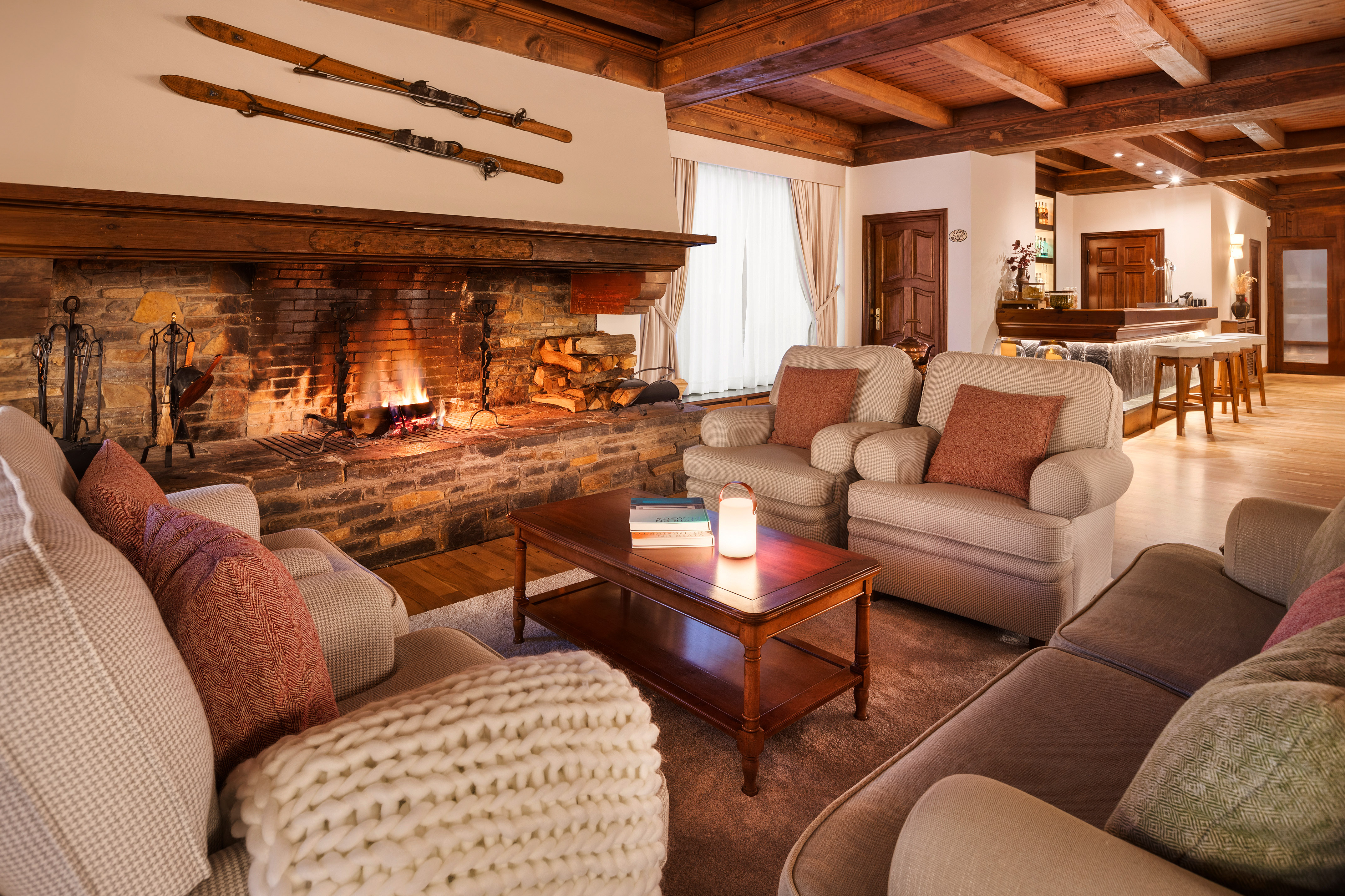 Warm ski lodge lounge with stone fireplace, vintage skis, and comfortable seating.