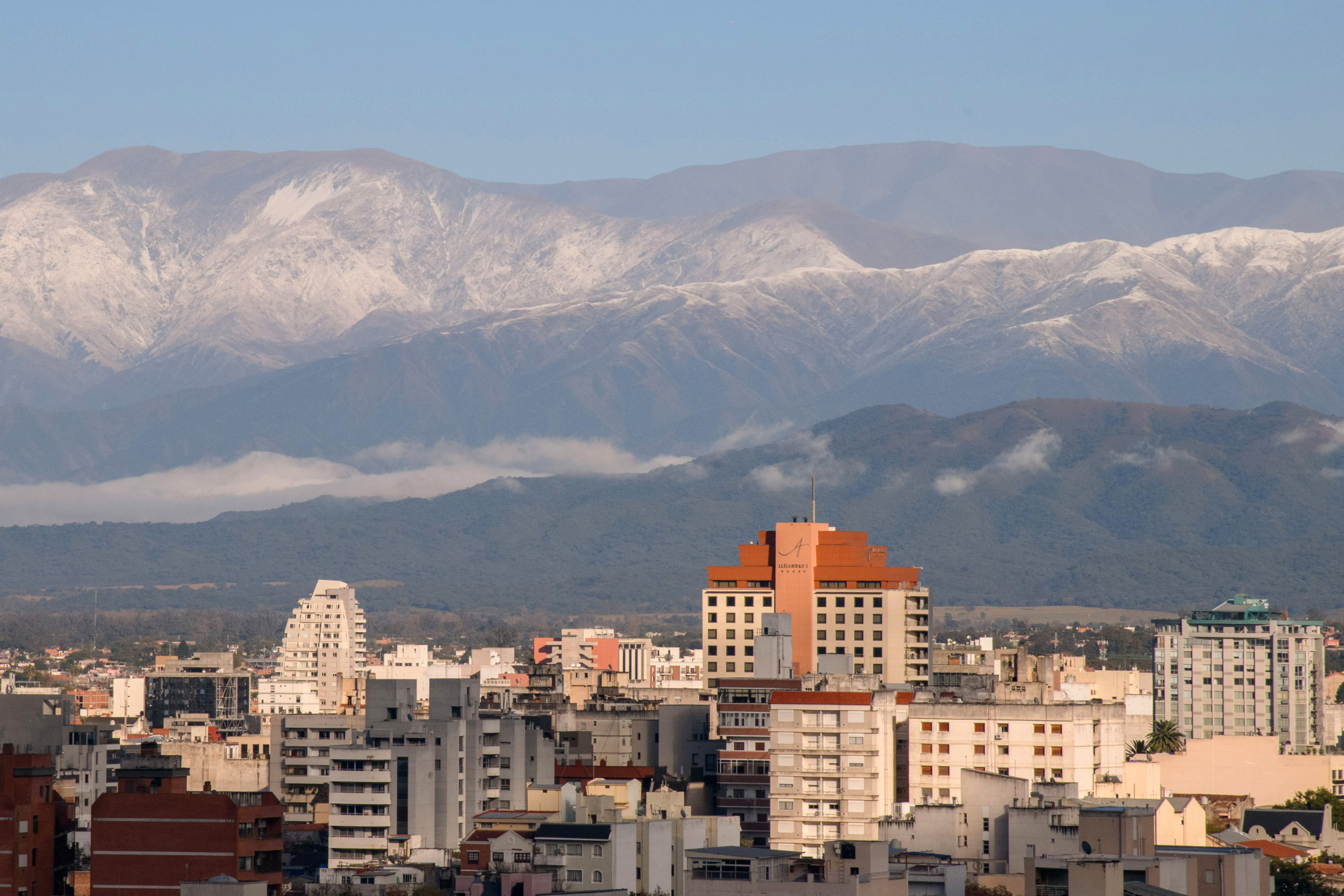 Urban buildings with prominent orange hotel, backed by snow-capped mountains.