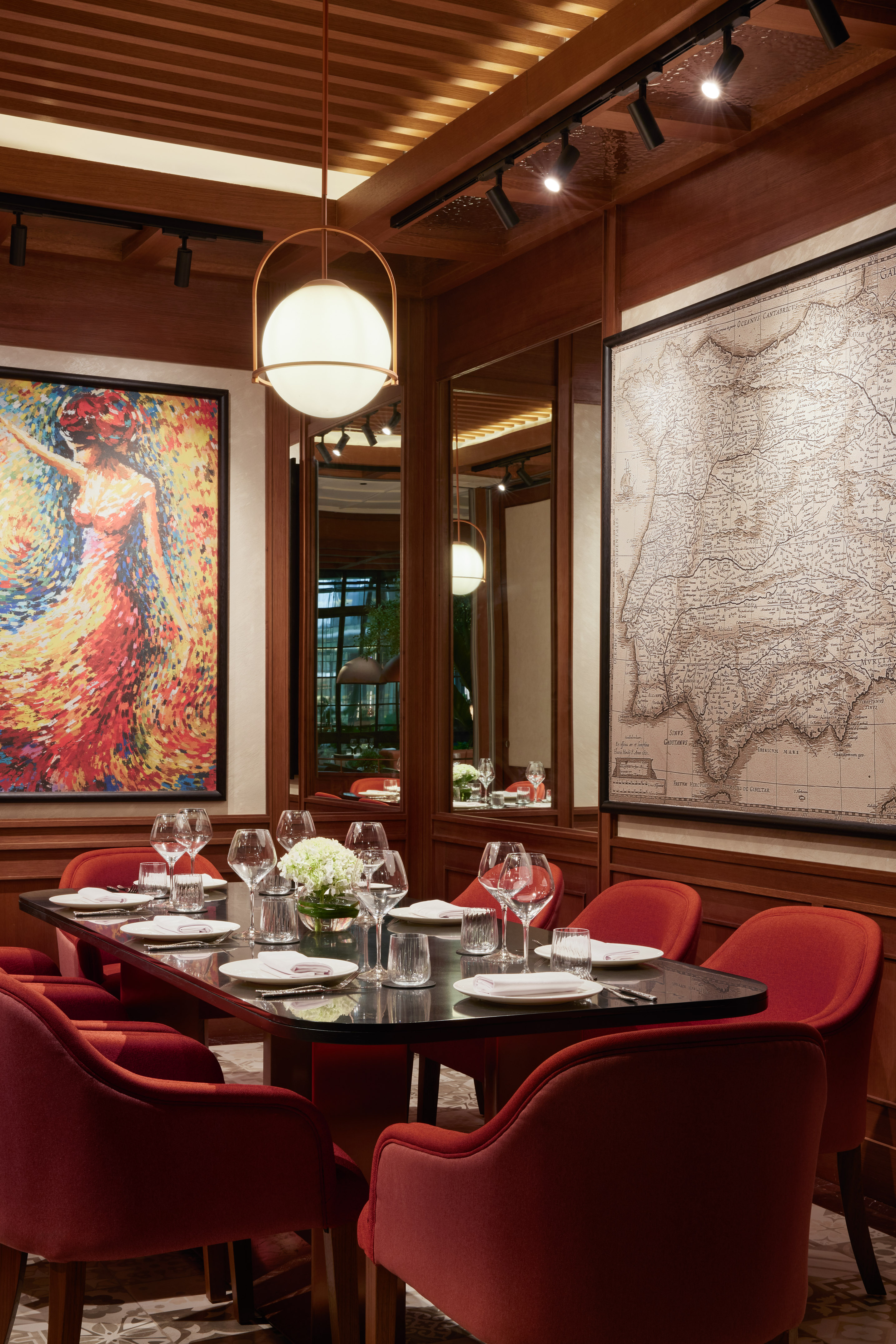 Chic restaurant dining room with red chairs, set table, colorful art, and vintage map.