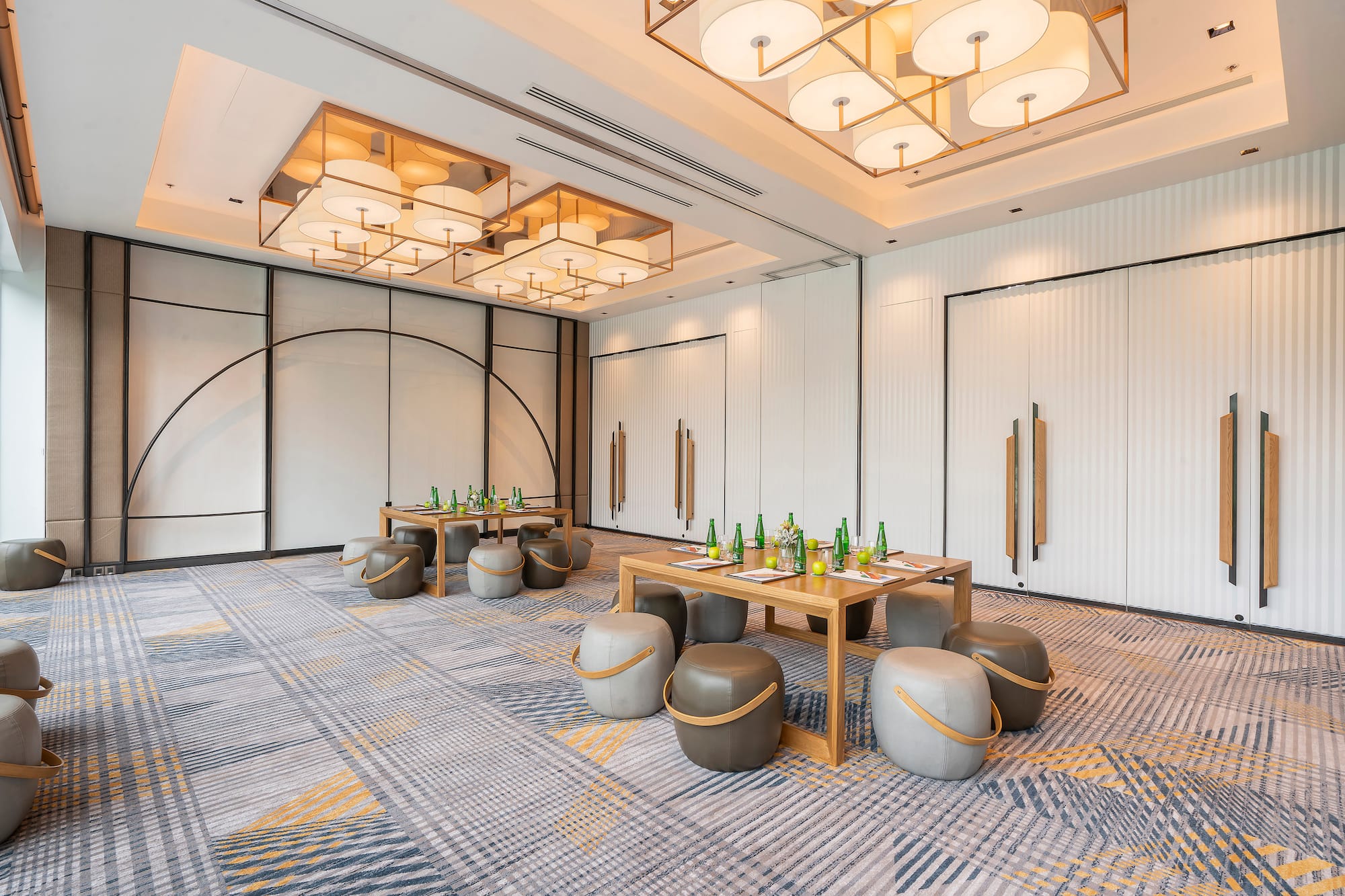 Modern meeting room with wooden tables, ottomans, and elegant lighting.