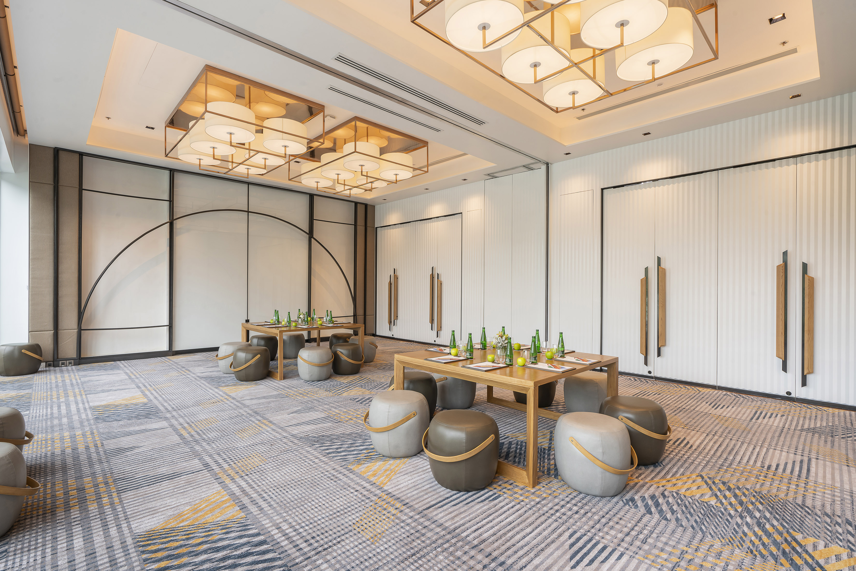Modern meeting room with wooden tables, ottomans, and elegant lighting.