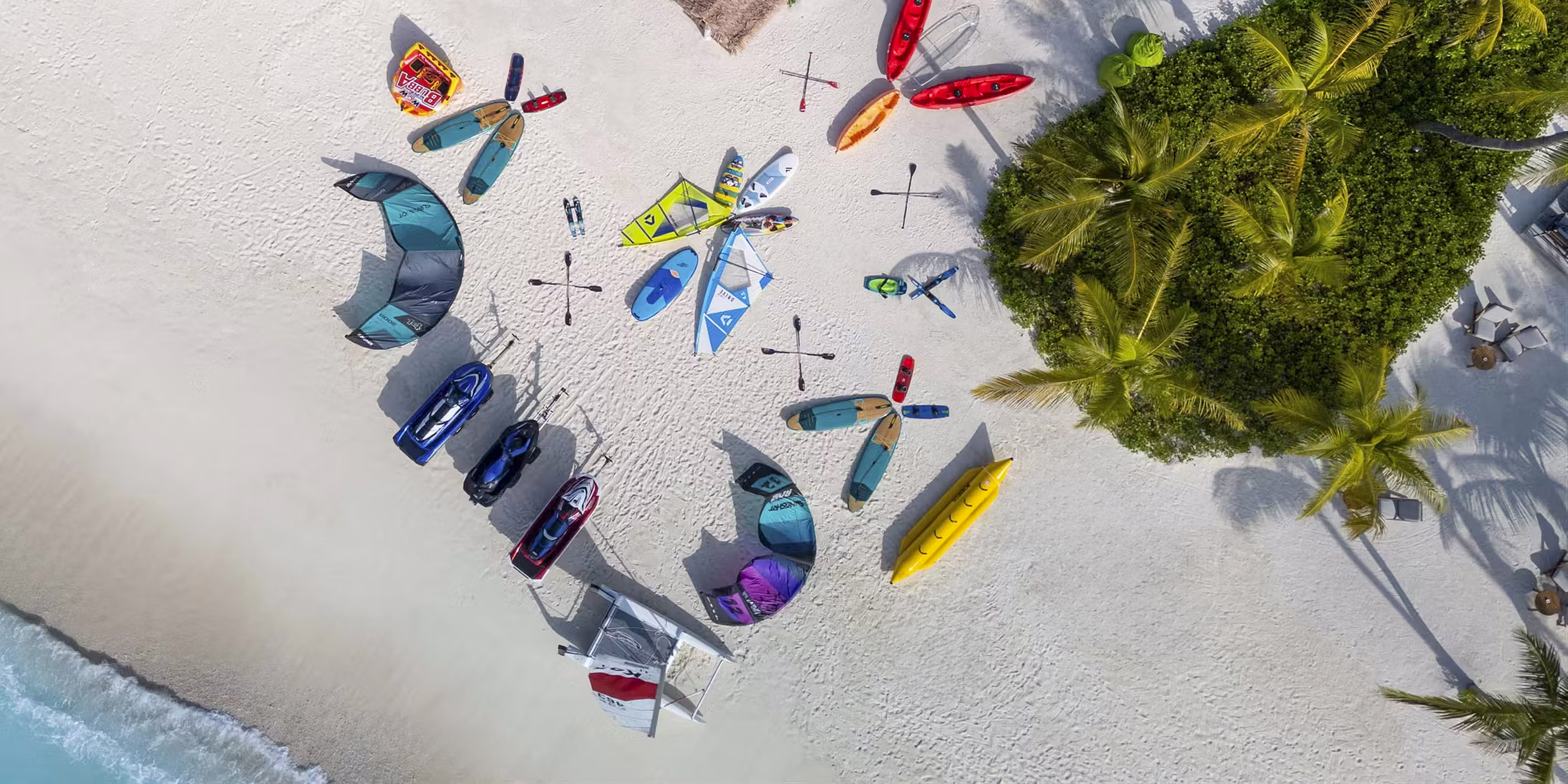 Tropical resort beach: water sports gear including kayaks, jet skis, and kites.