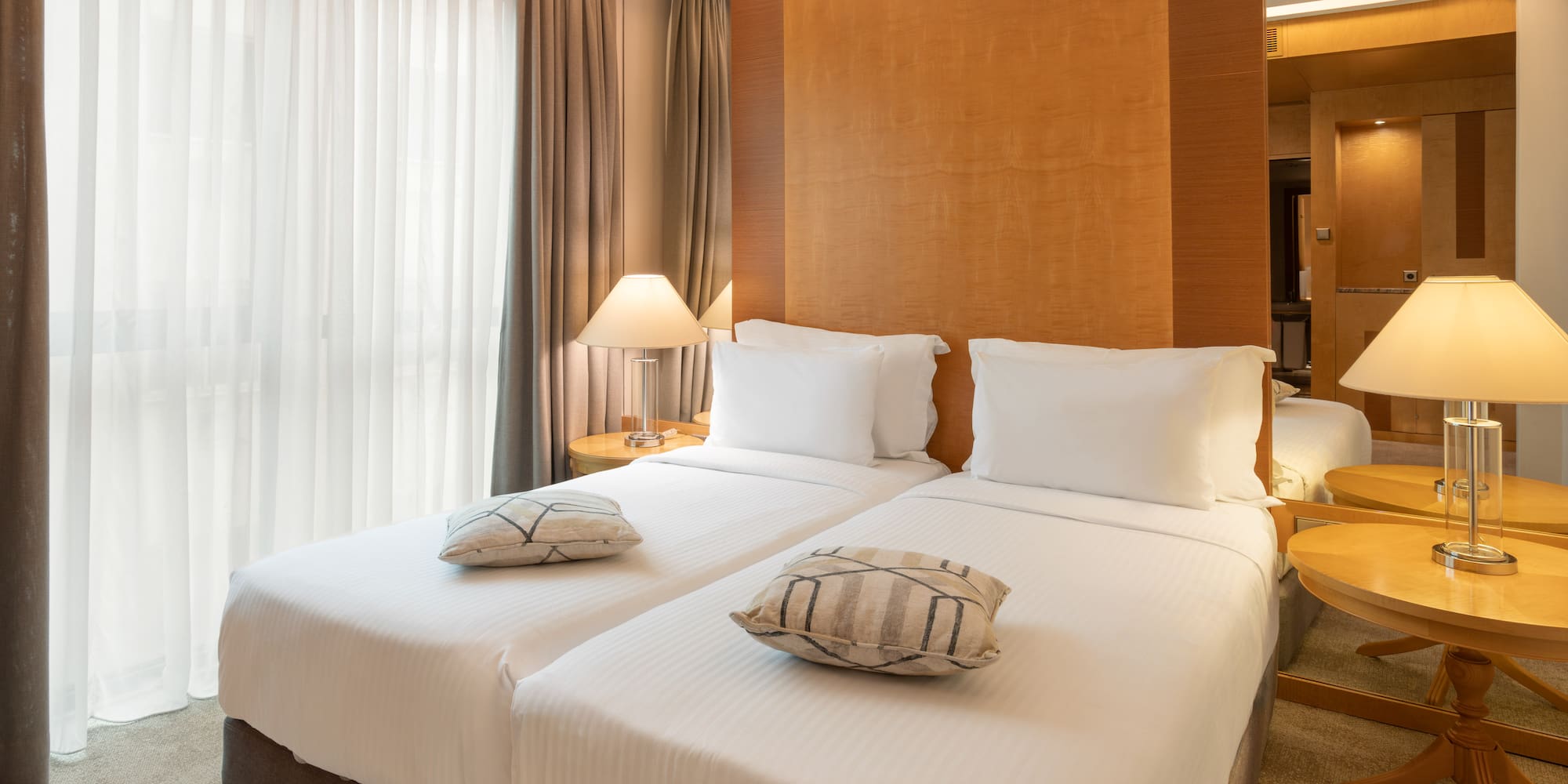 Two twin beds with white linens in a modern hotel room, featuring bedside lamps.