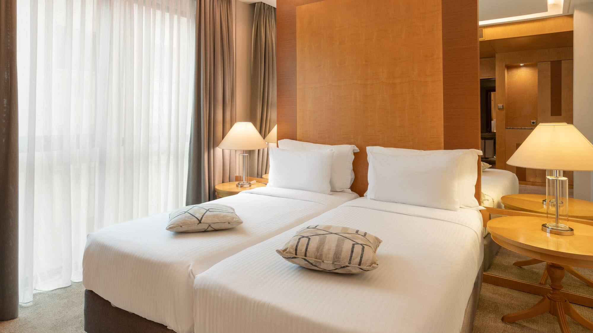 Two twin beds with white linens in a modern hotel room, featuring bedside lamps.