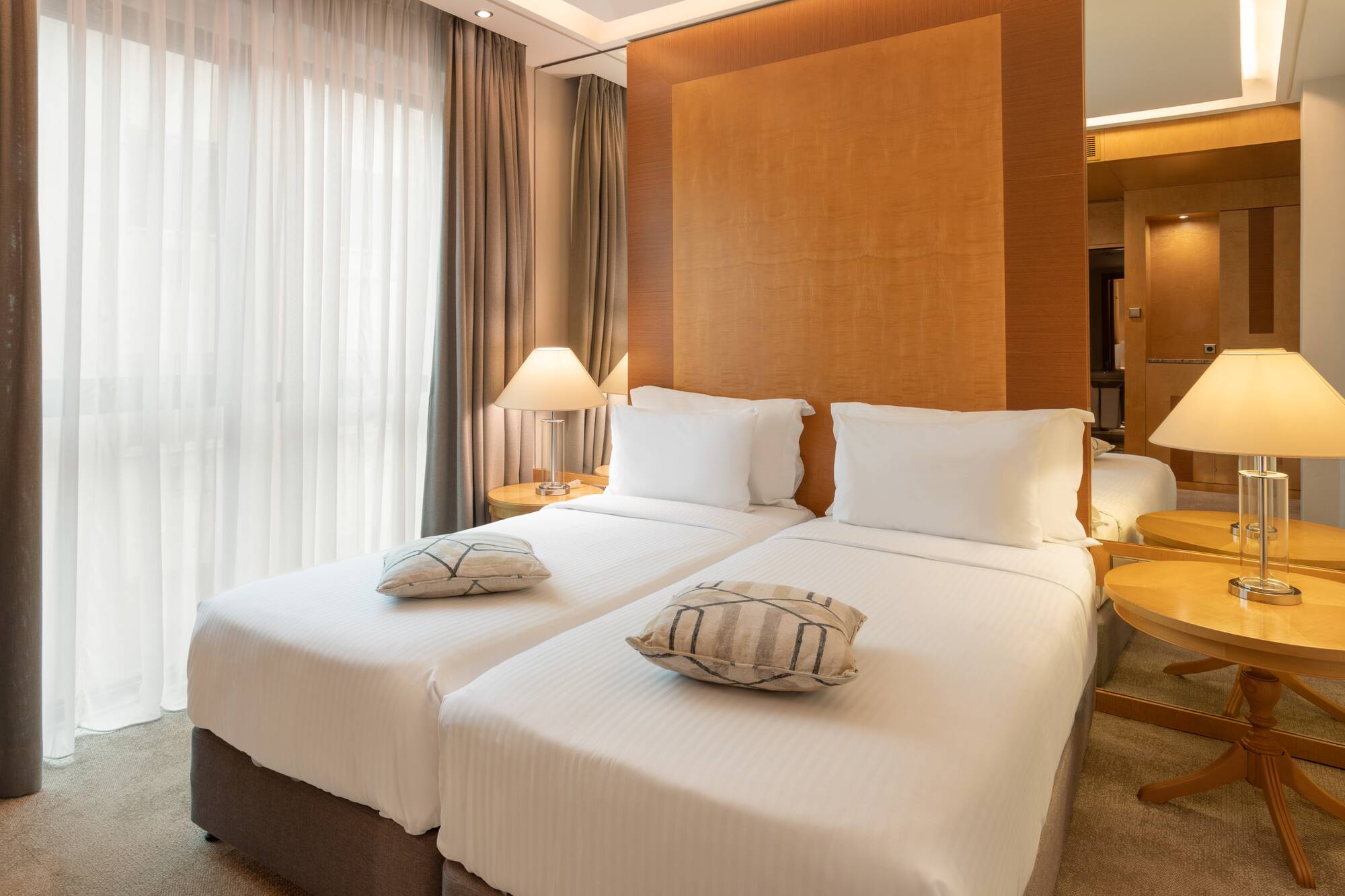 Two twin beds with white linens in a modern hotel room, featuring bedside lamps.