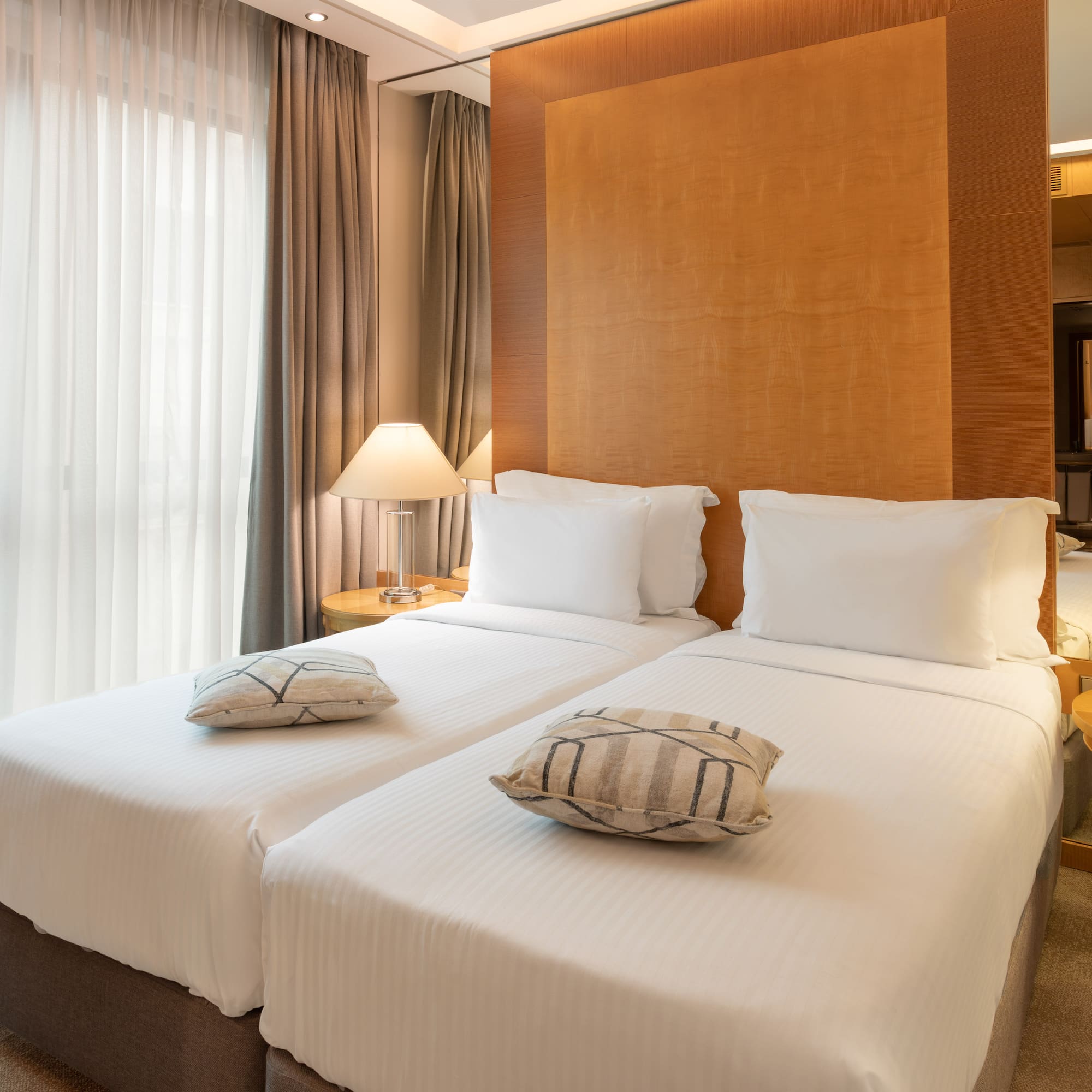 Two twin beds with white linens in a modern hotel room, featuring bedside lamps.