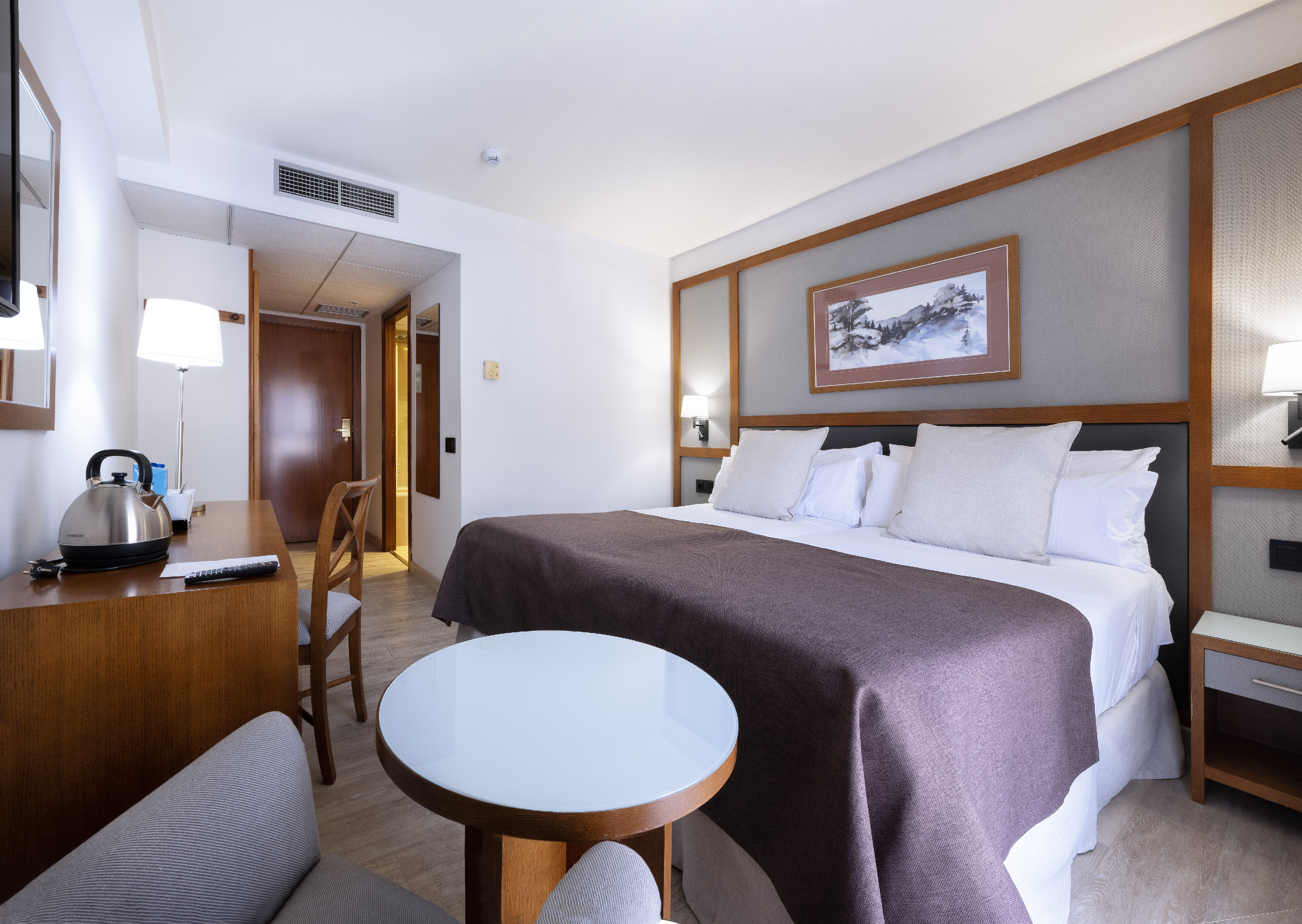 Modern hotel room with large bed, desk, kettle, and contemporary decor.