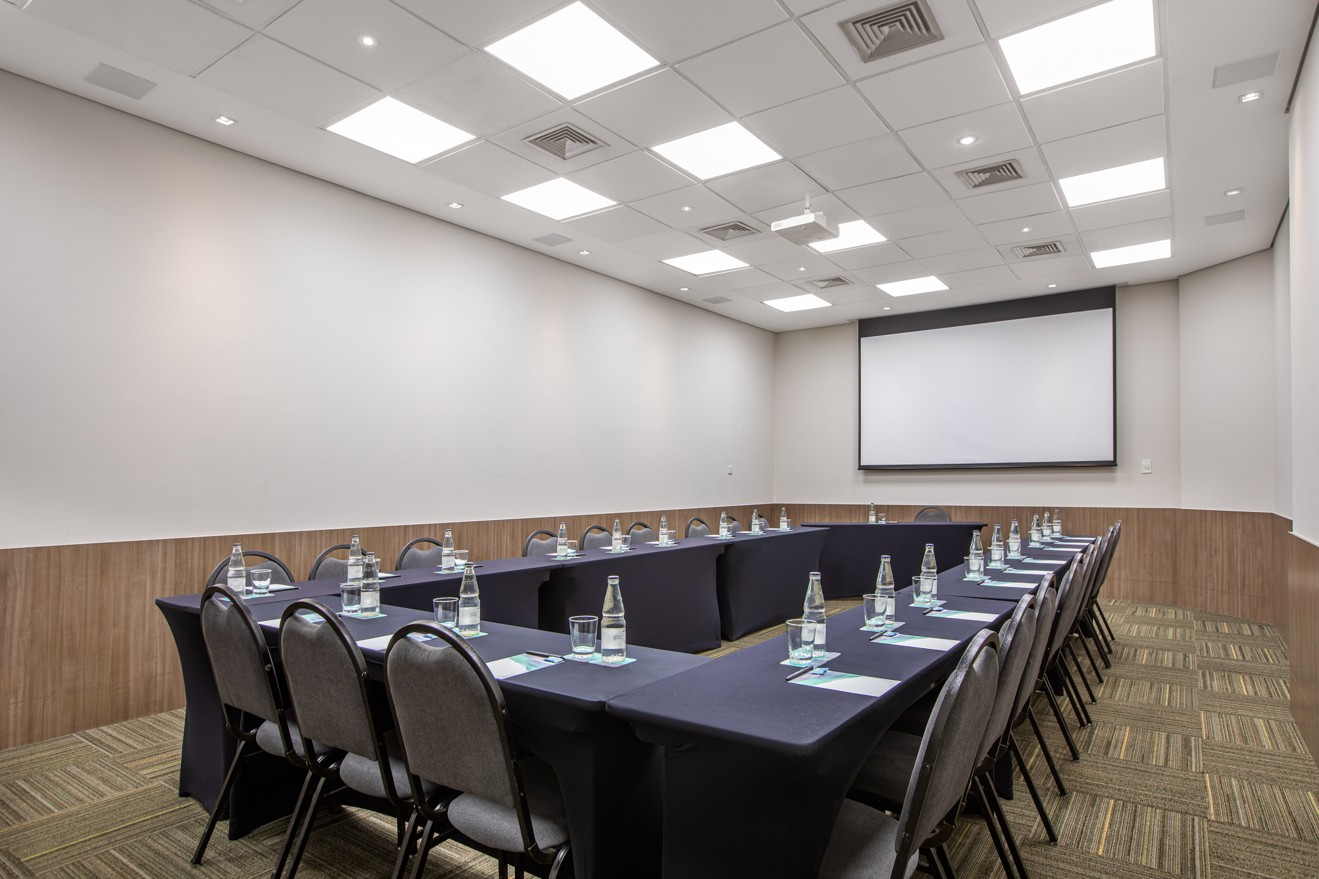 Modern conference room with U-shaped table setup, projection screen, and chairs.