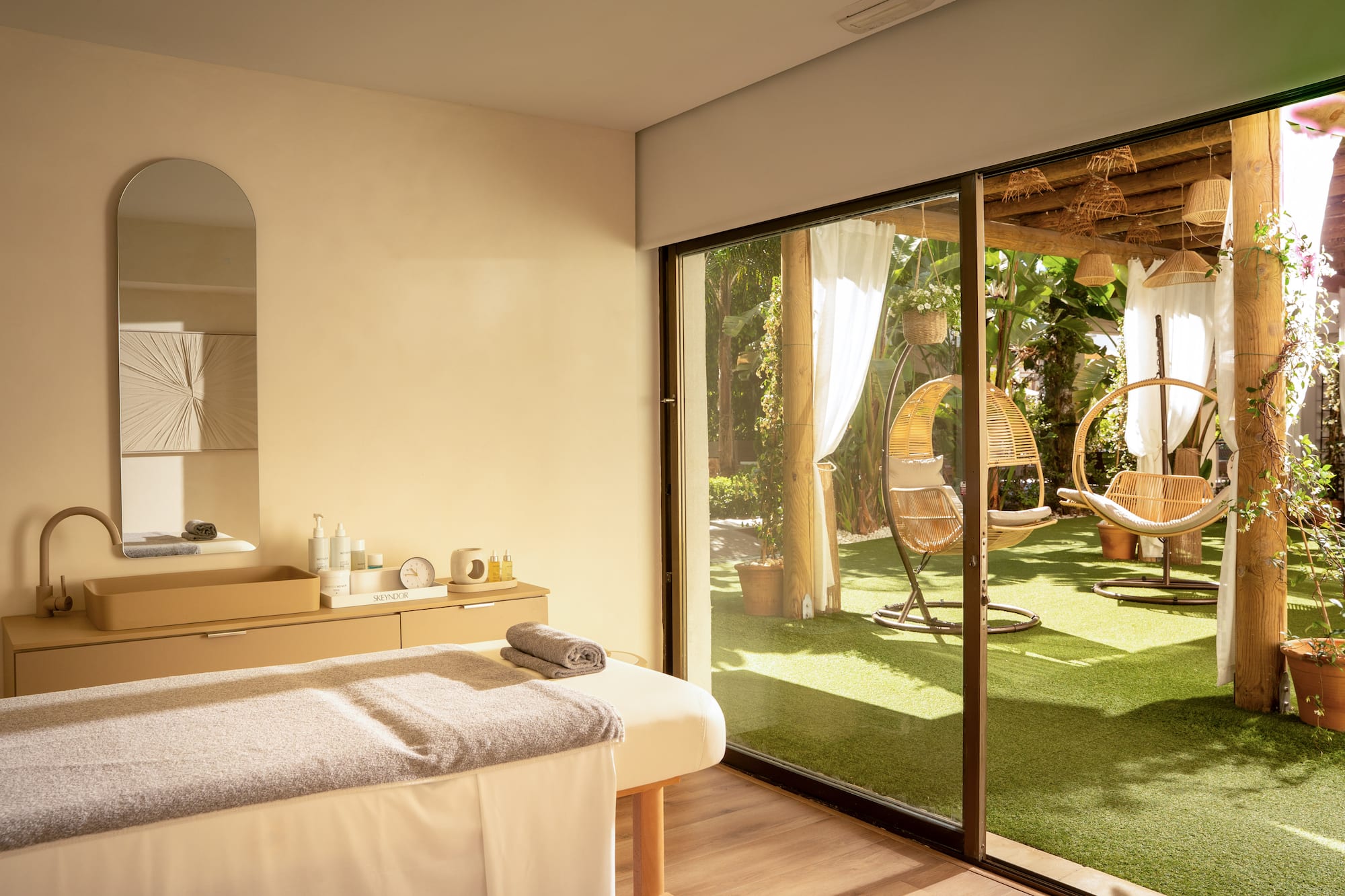Camilla de masaje en sala de spa con vista a jardín con sillas colgantes.