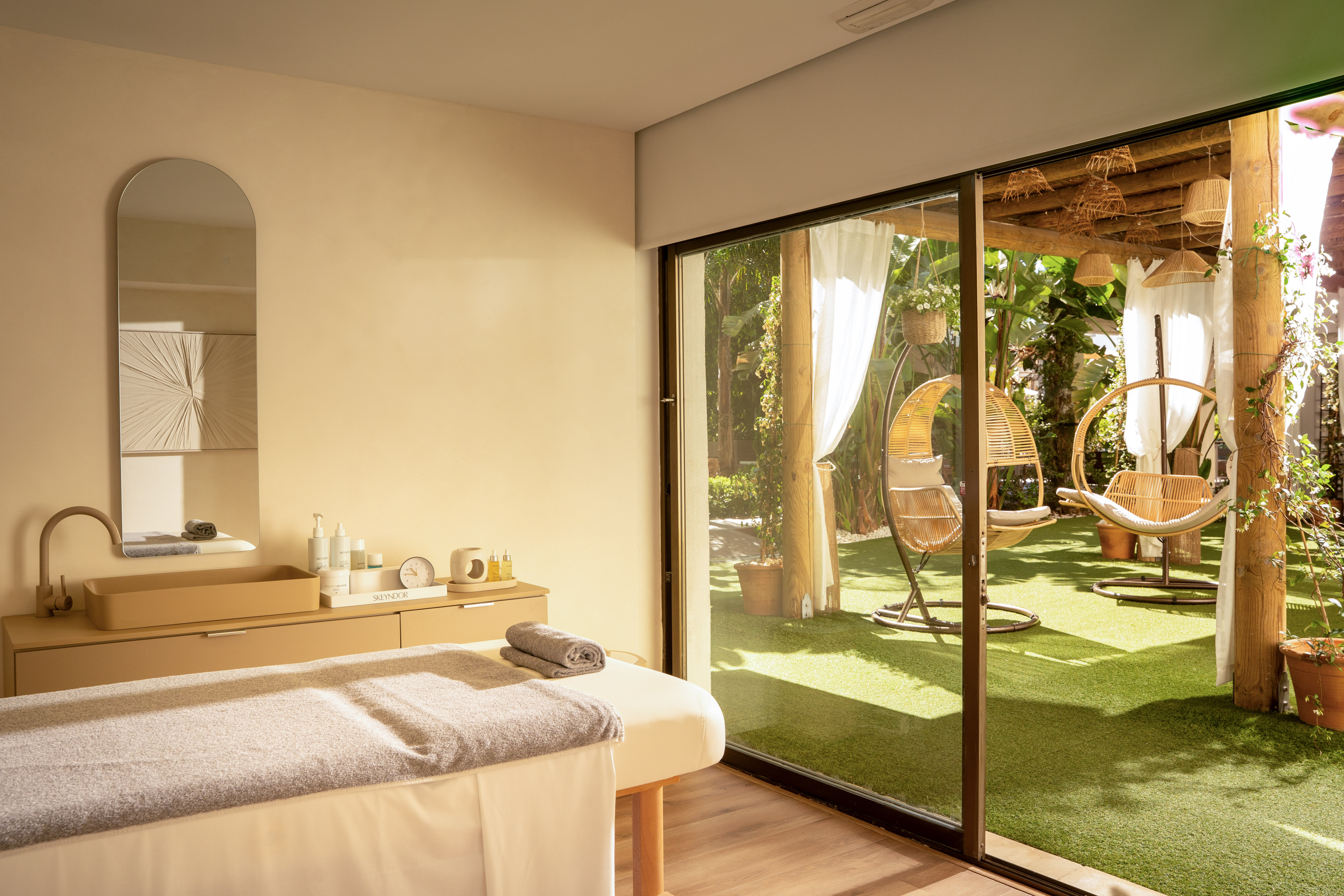 Camilla de masaje en sala de spa con vista a jardín con sillas colgantes.