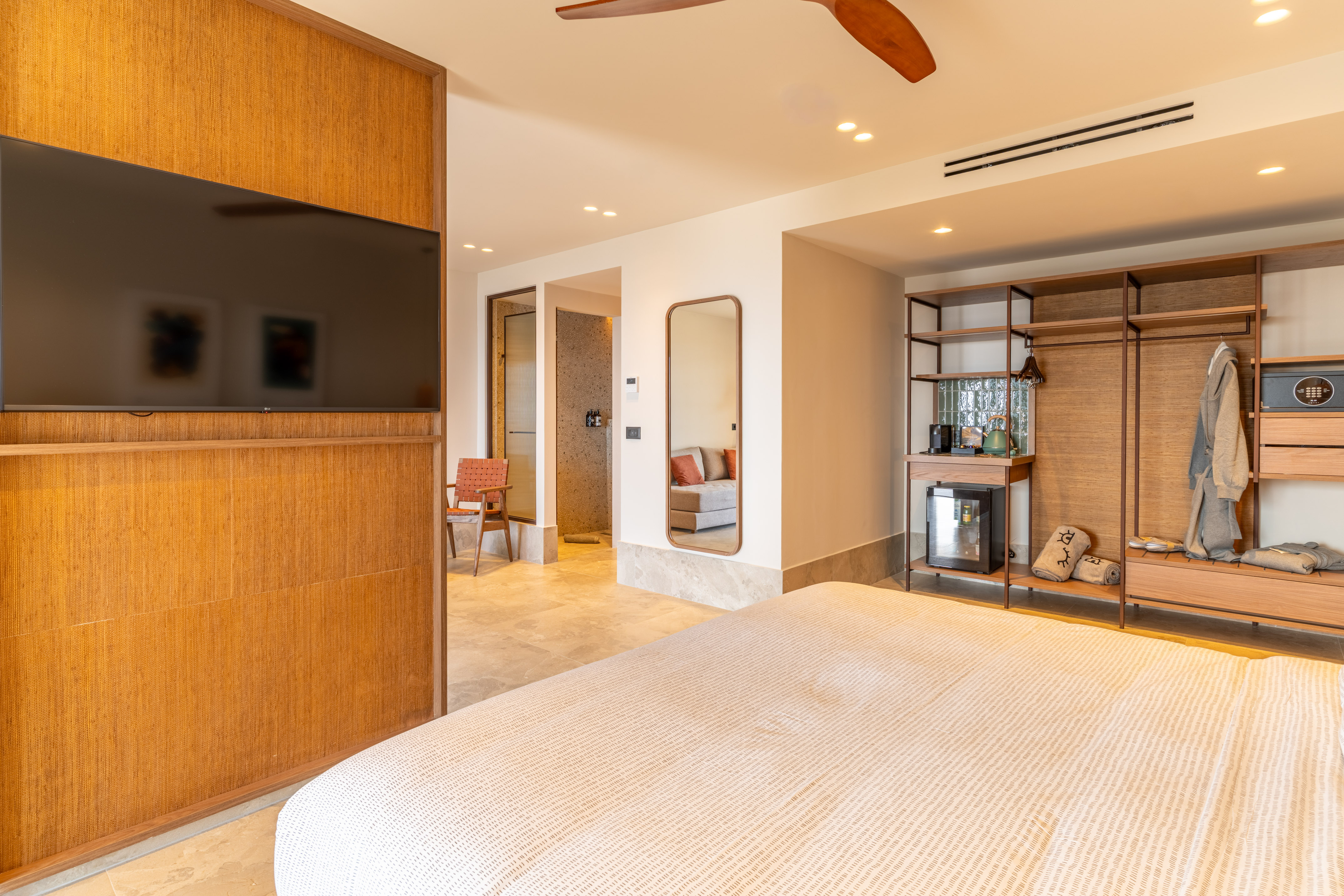 Modern hotel room with bed, large TV on woven wall, and open wardrobe.