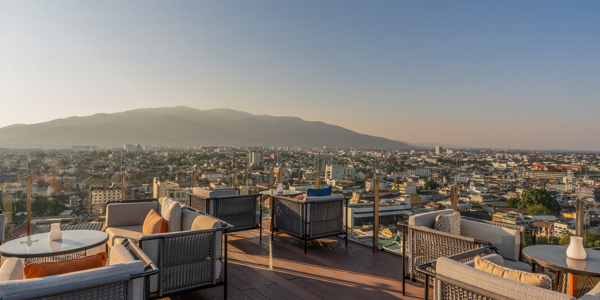 a rooftop patio with chairs and tables and a city in the background