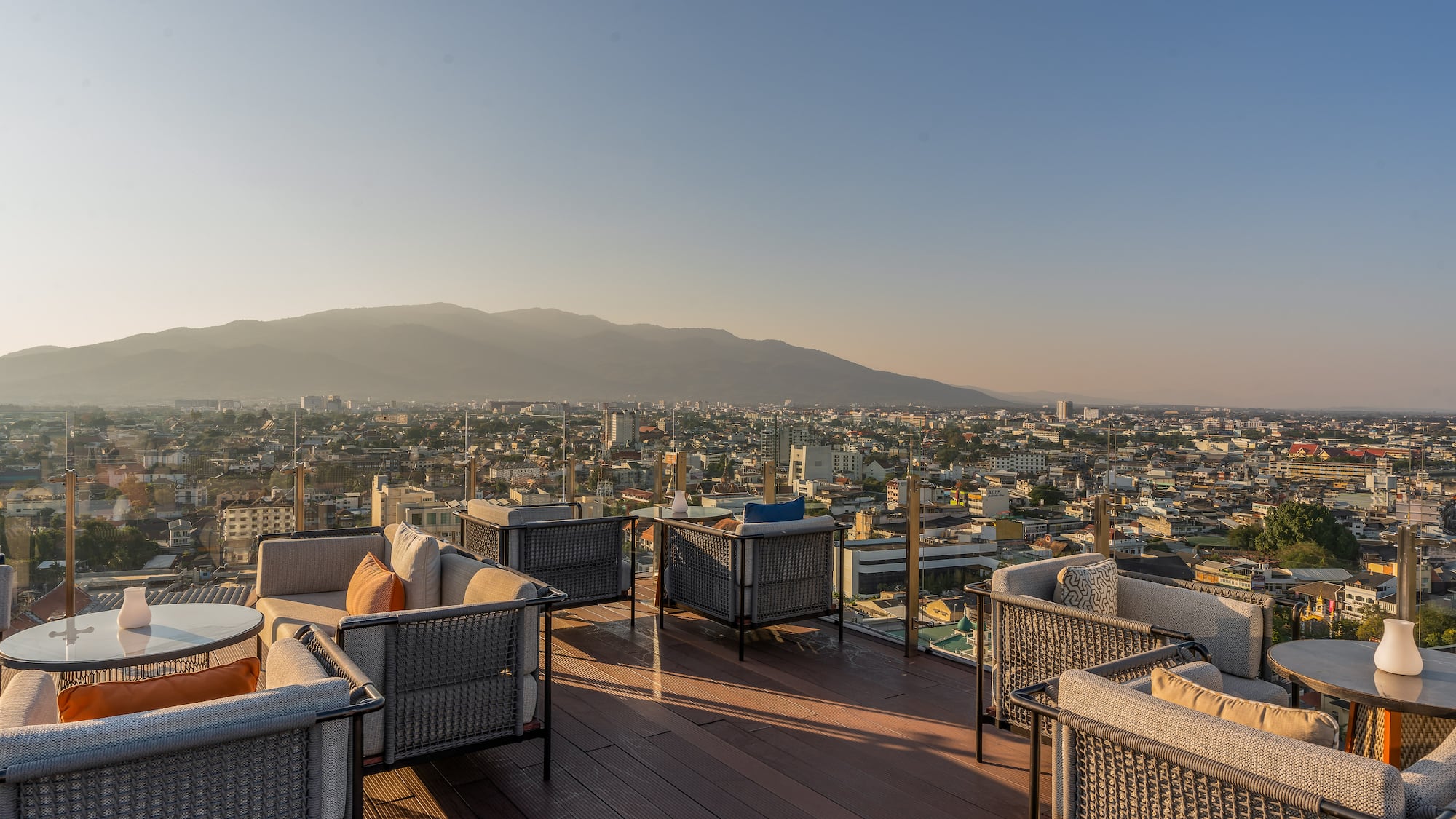 a rooftop patio with chairs and tables and a city in the background