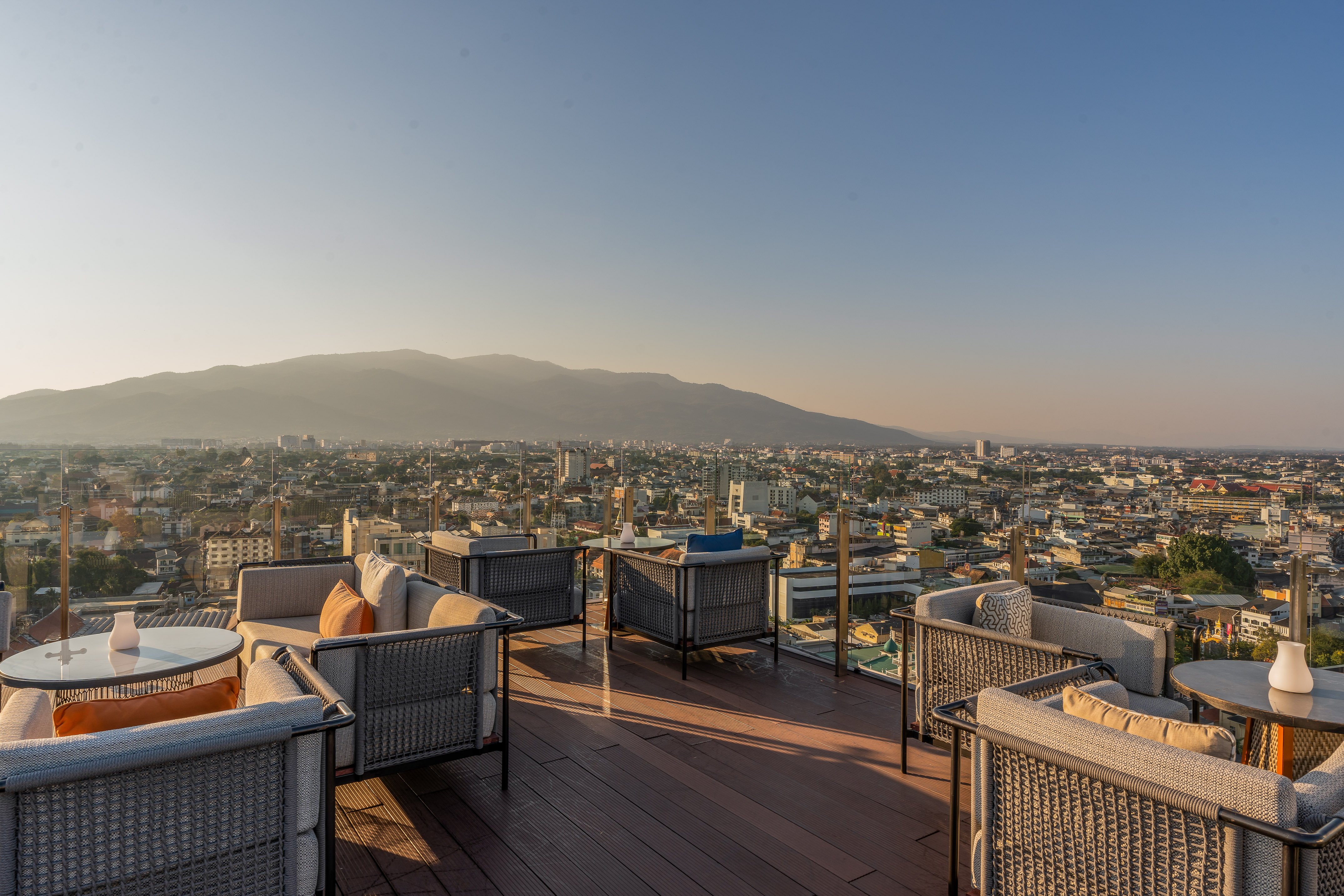 a rooftop patio with chairs and tables and a city in the background