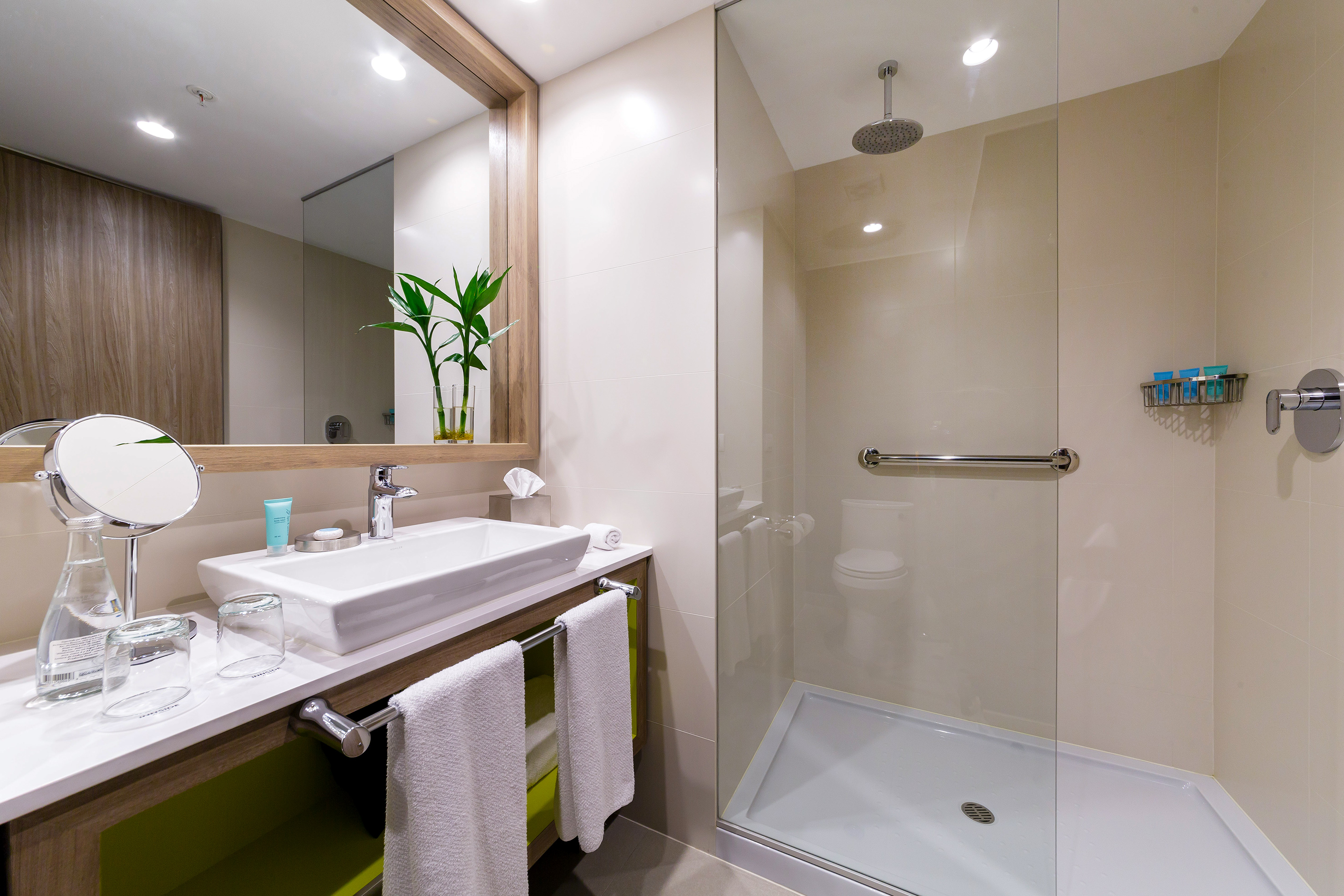 Modern hotel bathroom with vanity, white sink, and glass shower with rainfall head.