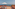 Terracotta rooftop terrace with ocean view, two sun loungers, and white sun umbrella.