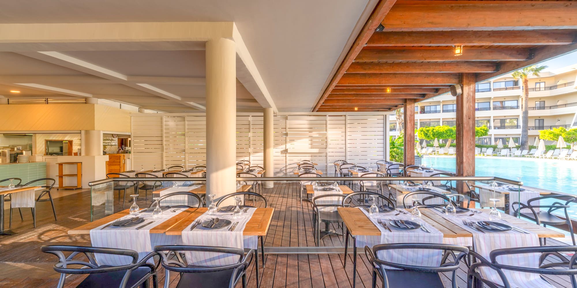 Poolside resort restaurant terrace with wooden deck and set dining tables.