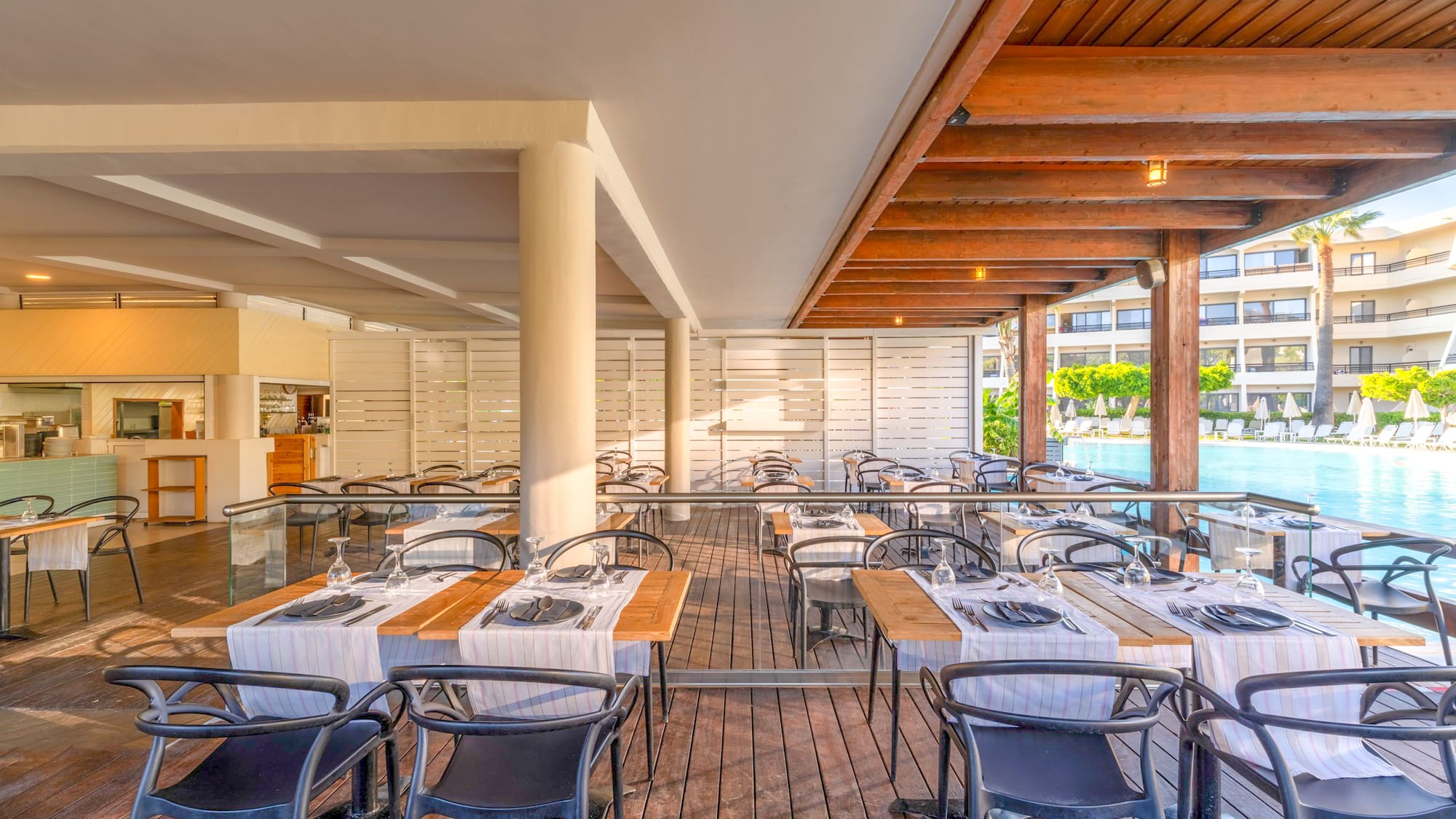 Poolside resort restaurant terrace with wooden deck and set dining tables.