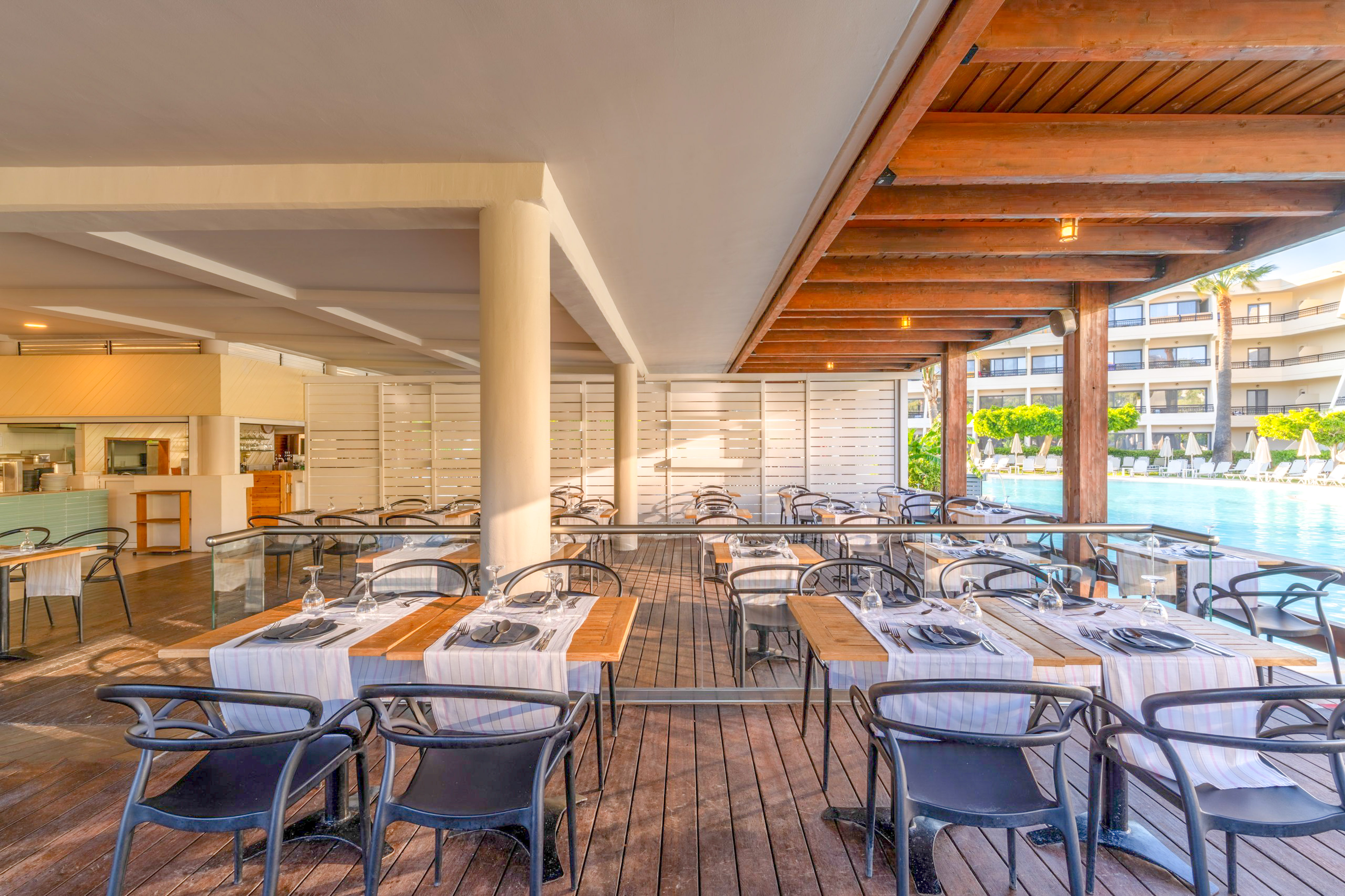 Poolside resort restaurant terrace with wooden deck and set dining tables.