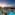 a pool with palm trees and a building with a beach and a sunset