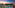a pool with palm trees and a building with a beach and a sunset