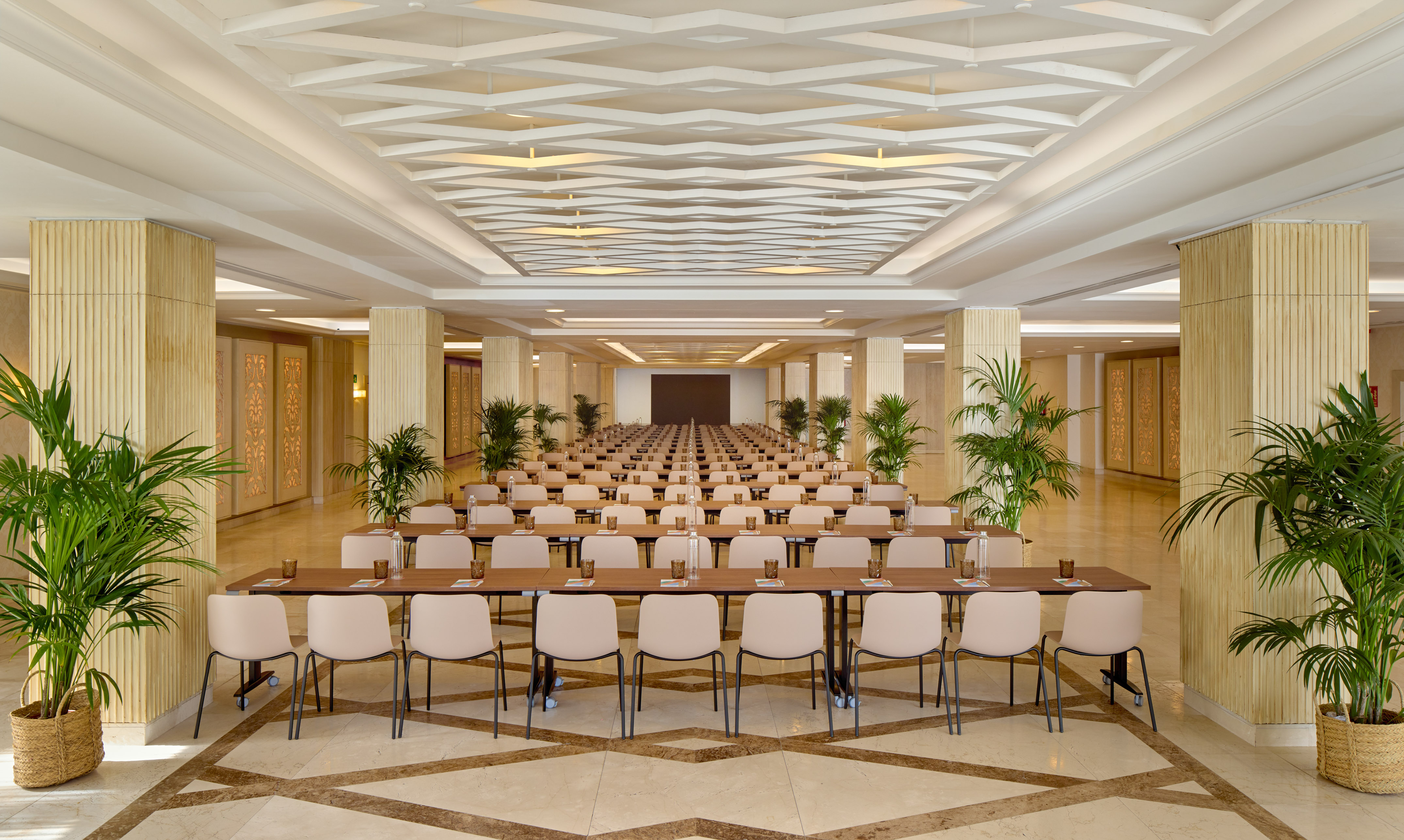 Elegant conference room with classroom seating, patterned ceiling, and plants.