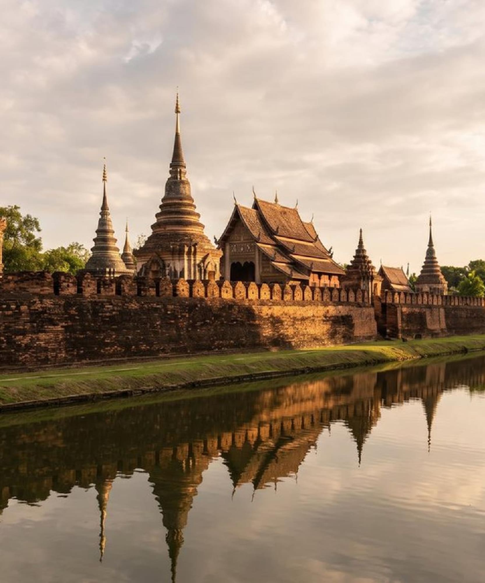 Estupas y templos de Sukhothai reflejados en el río al atardecer.