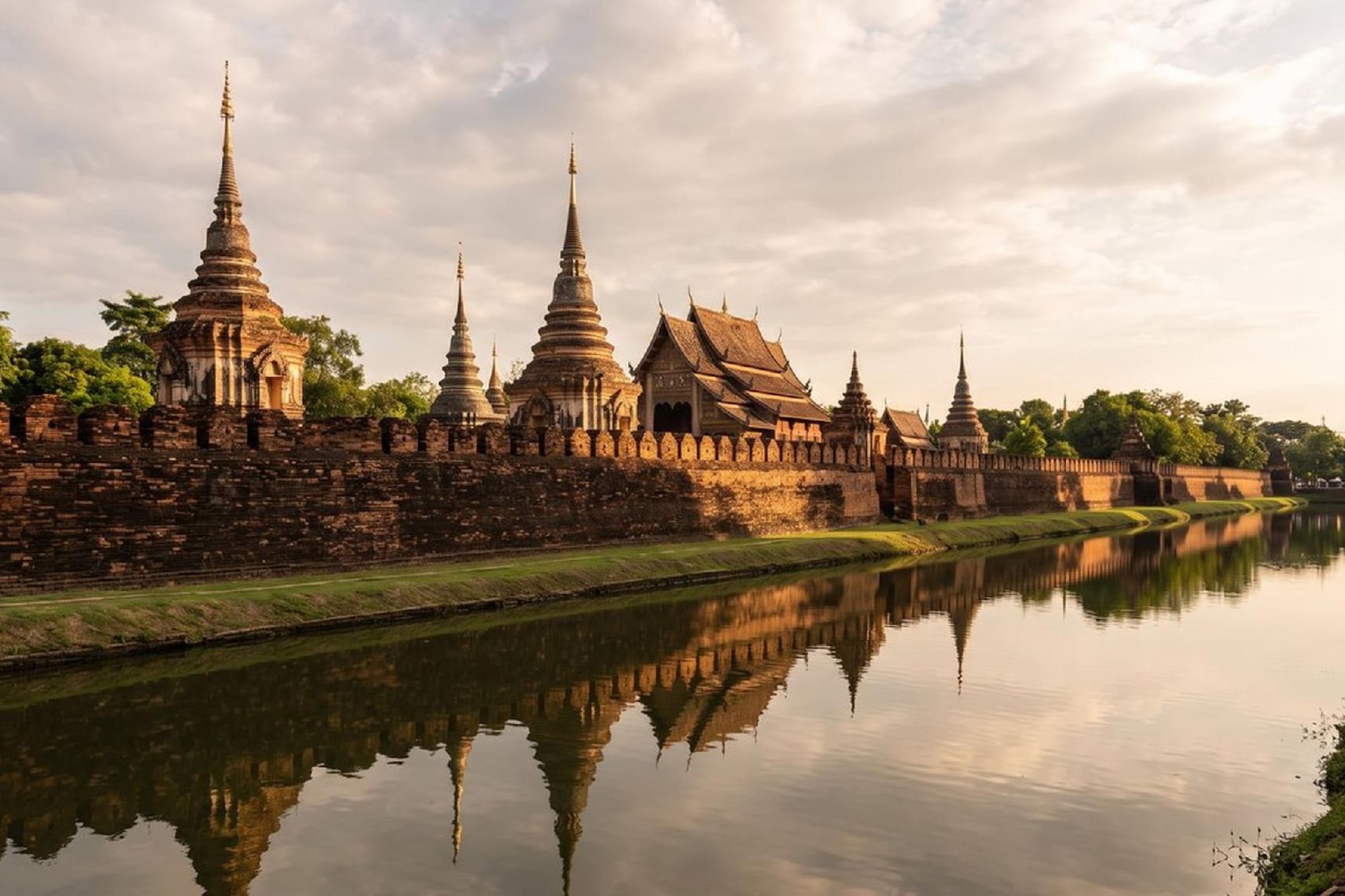 Estupas y templos de Sukhothai reflejados en el río al atardecer.