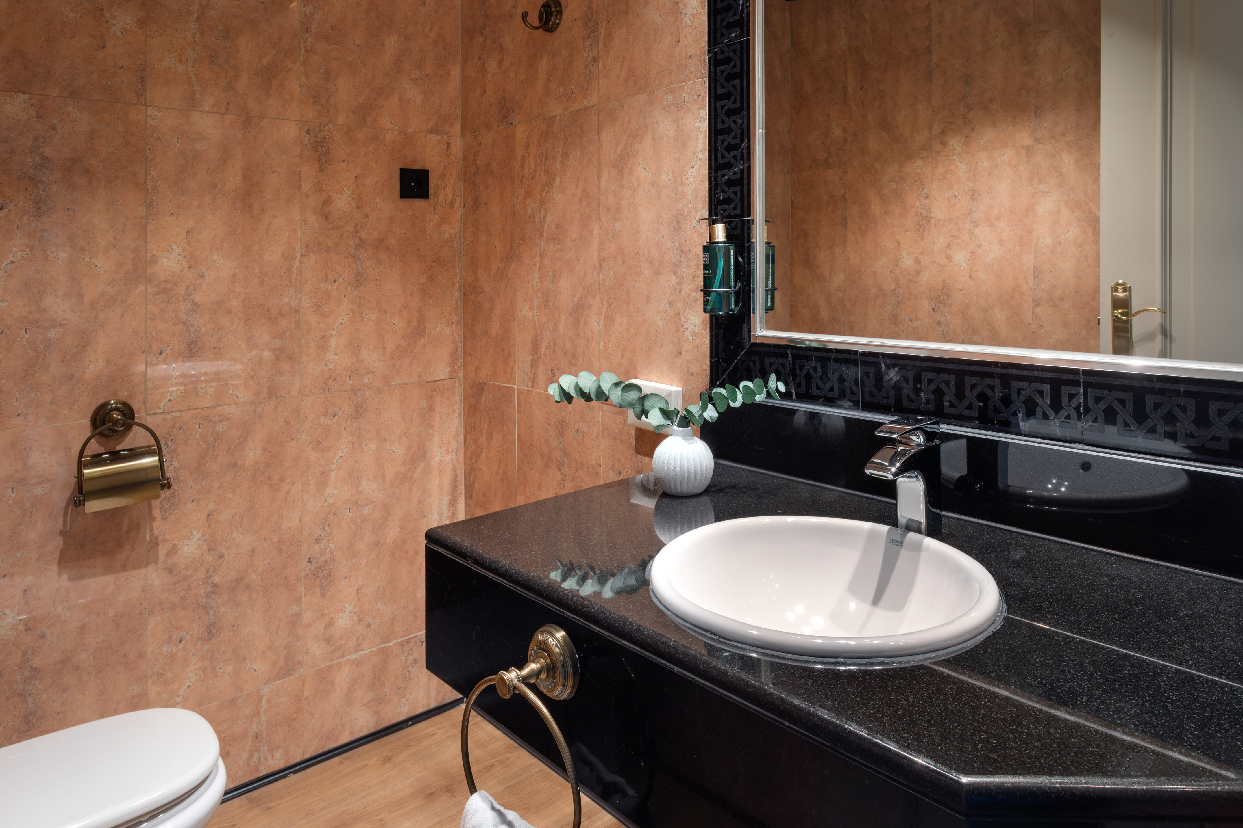 Black granite bathroom vanity with sink, mirror, and brown tiled walls.