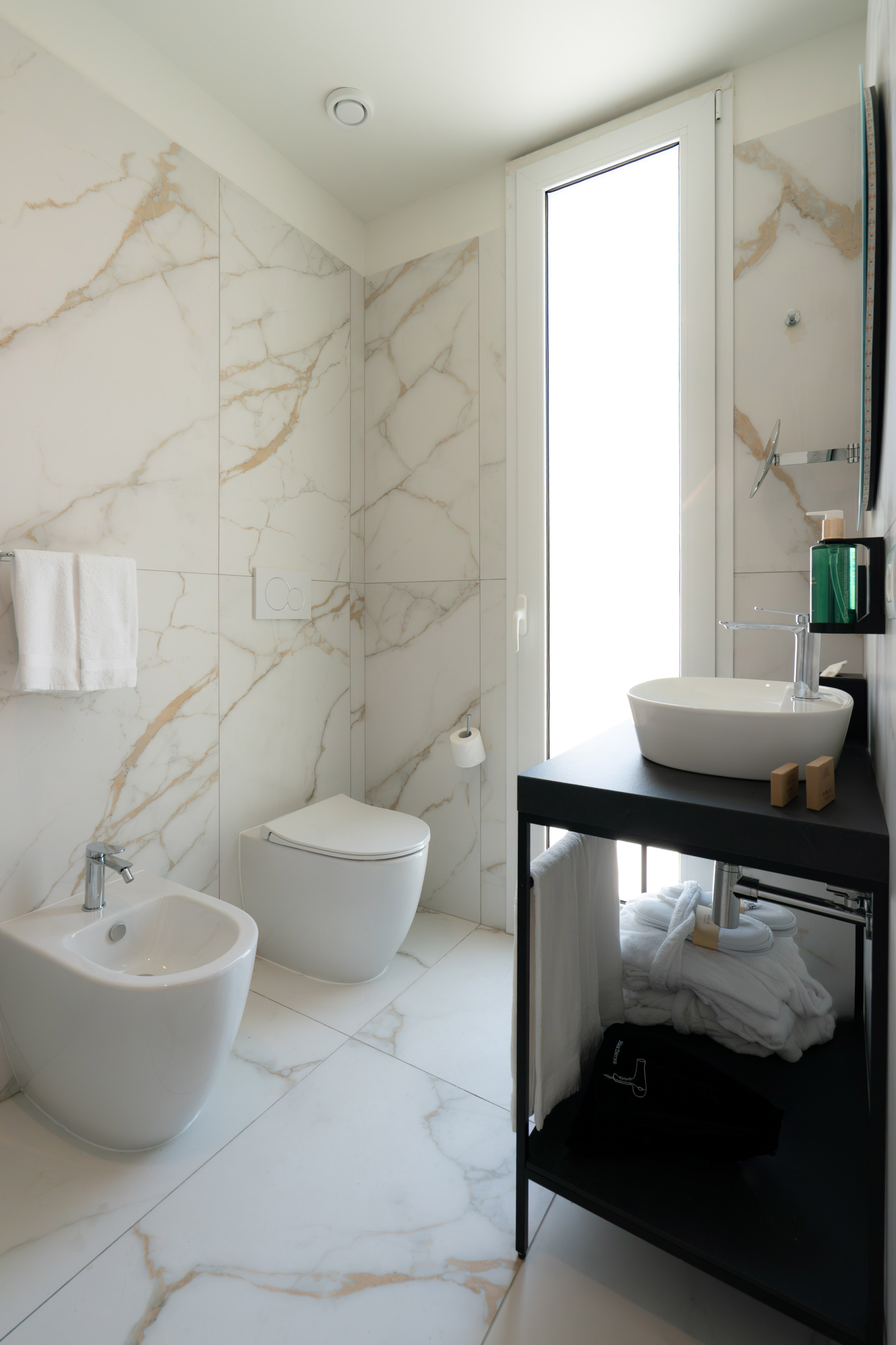 White marble bathroom with modern toilet, bidet, and dark vanity sink.