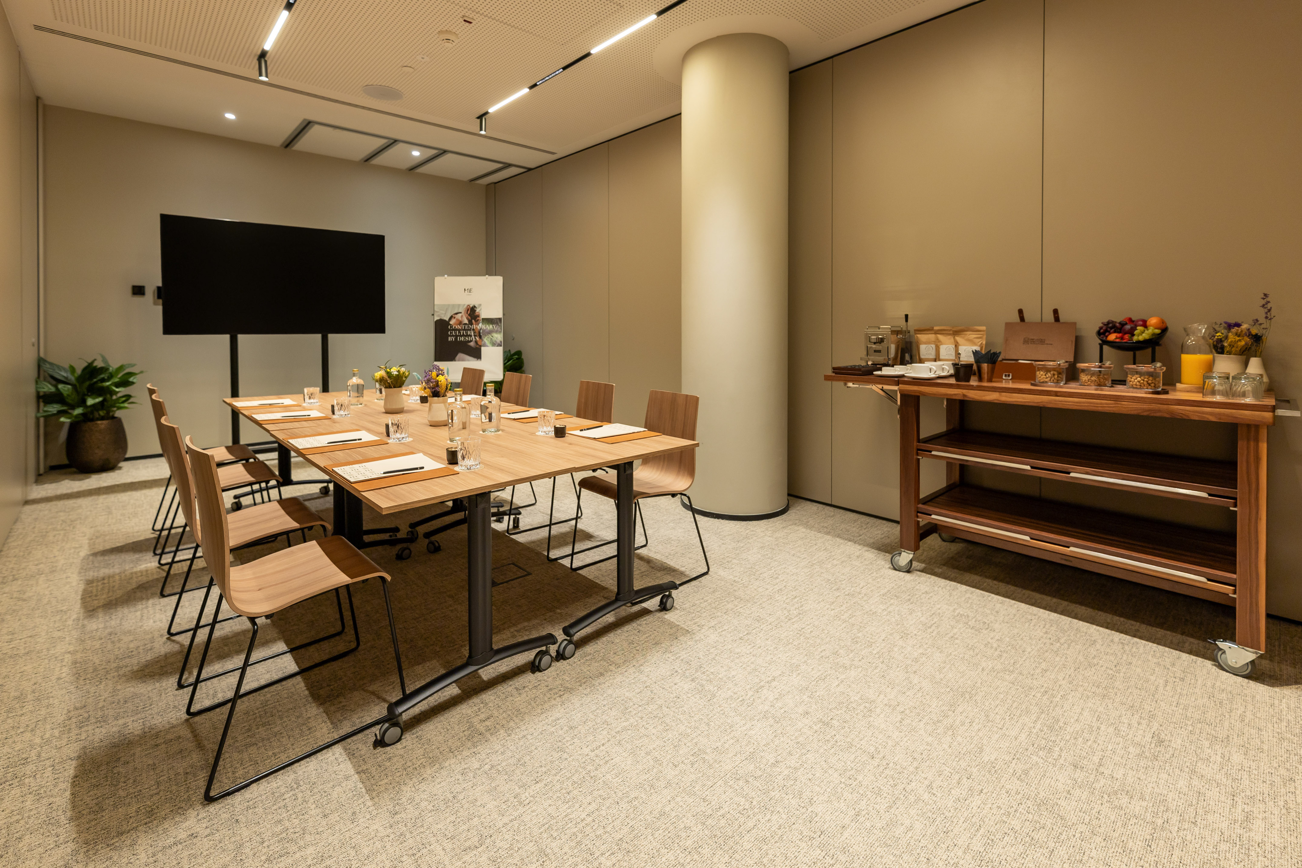 Modern meeting room with conference table, large screen, and refreshment bar.