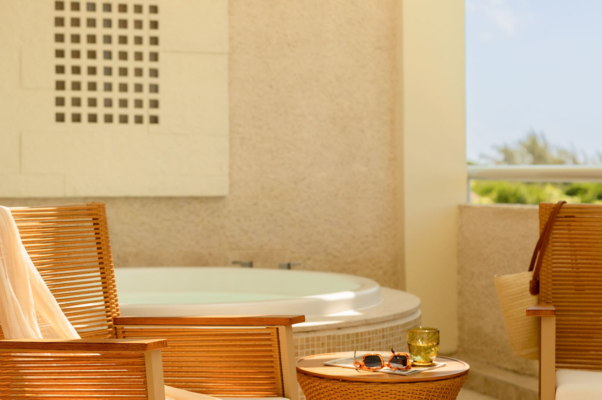 Sunny hotel balcony with hot tub, wooden rocking chair, and wicker table.