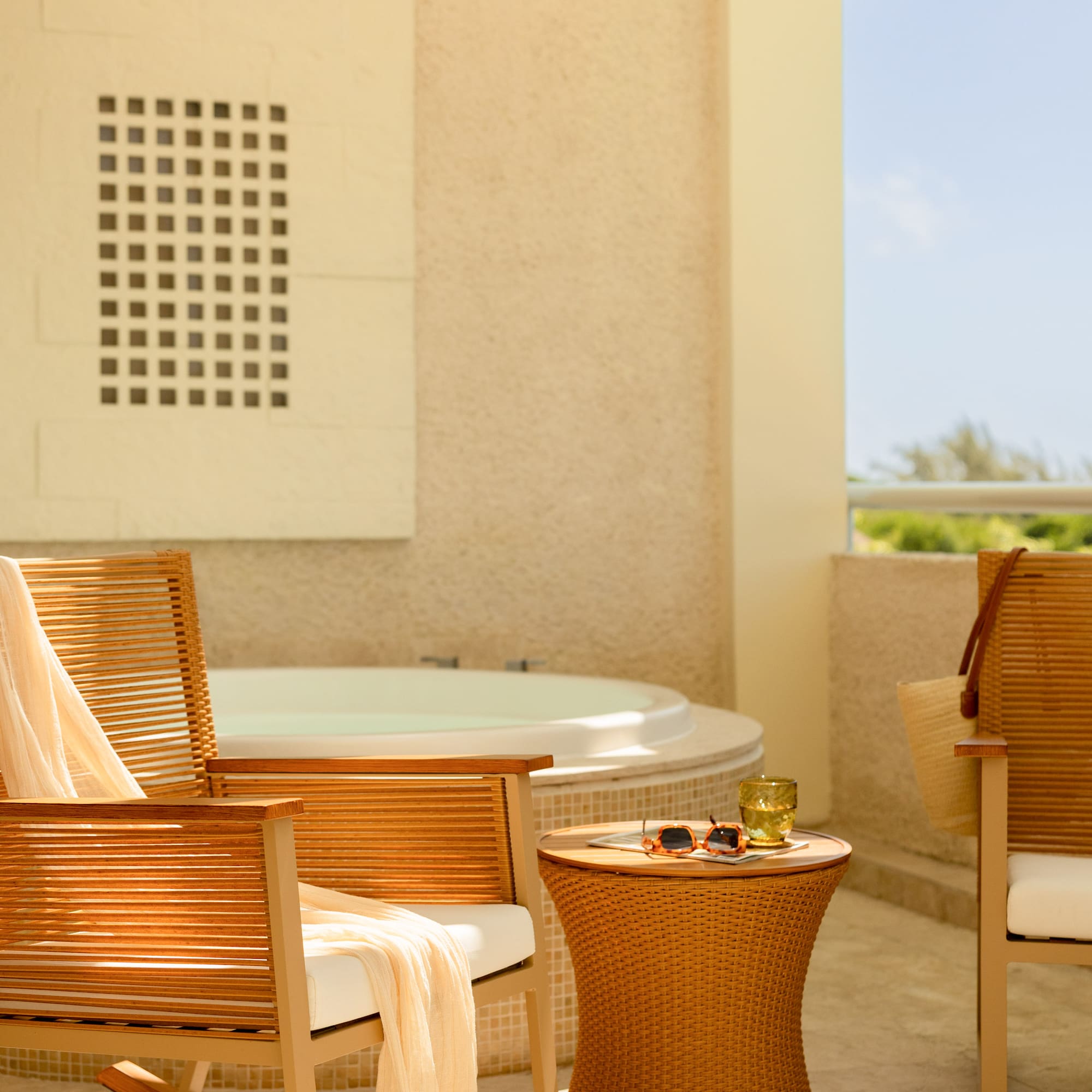 Sunny hotel balcony with hot tub, wooden rocking chair, and wicker table.