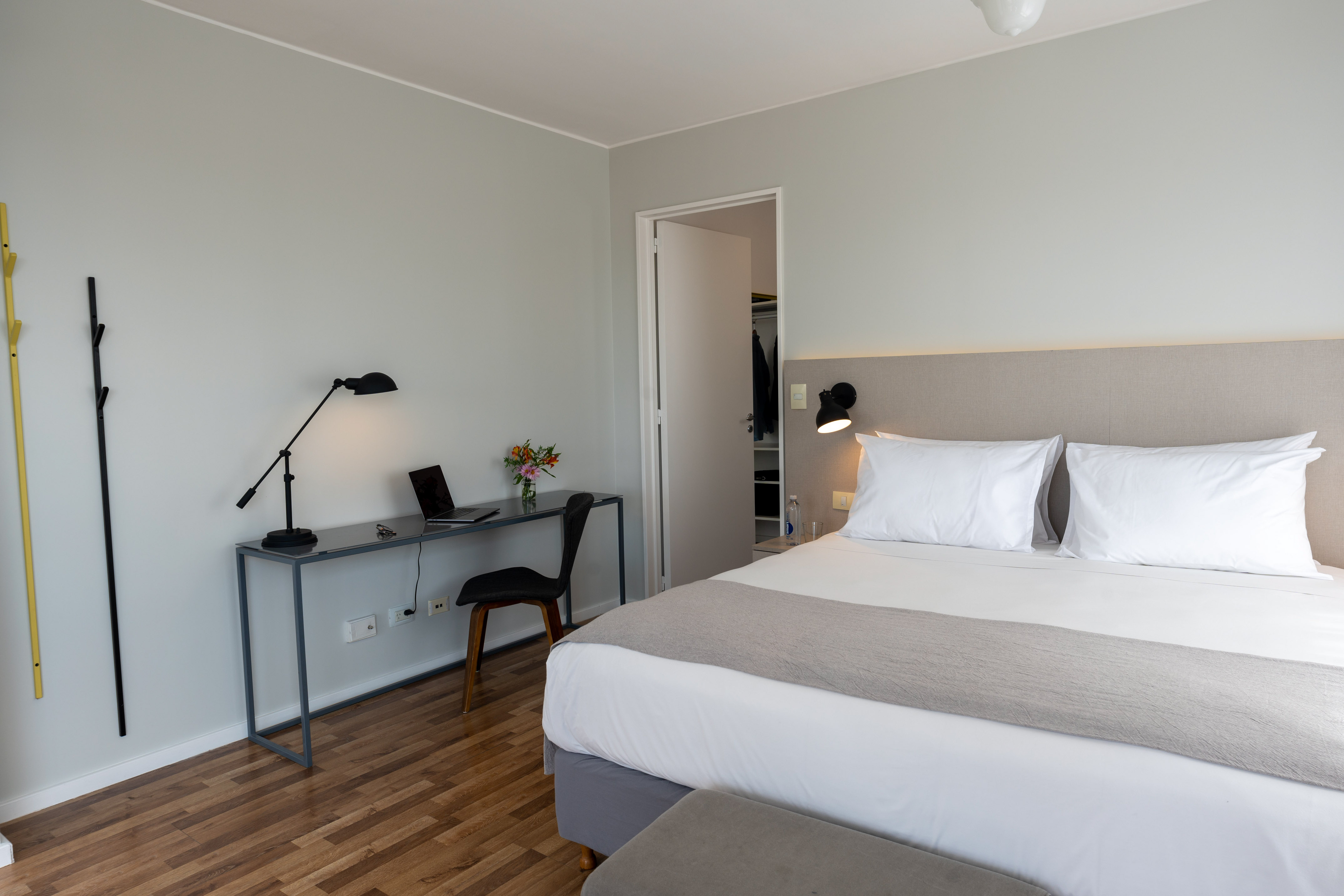 Modern hotel bedroom with bed, work desk, laptop, and wood flooring.