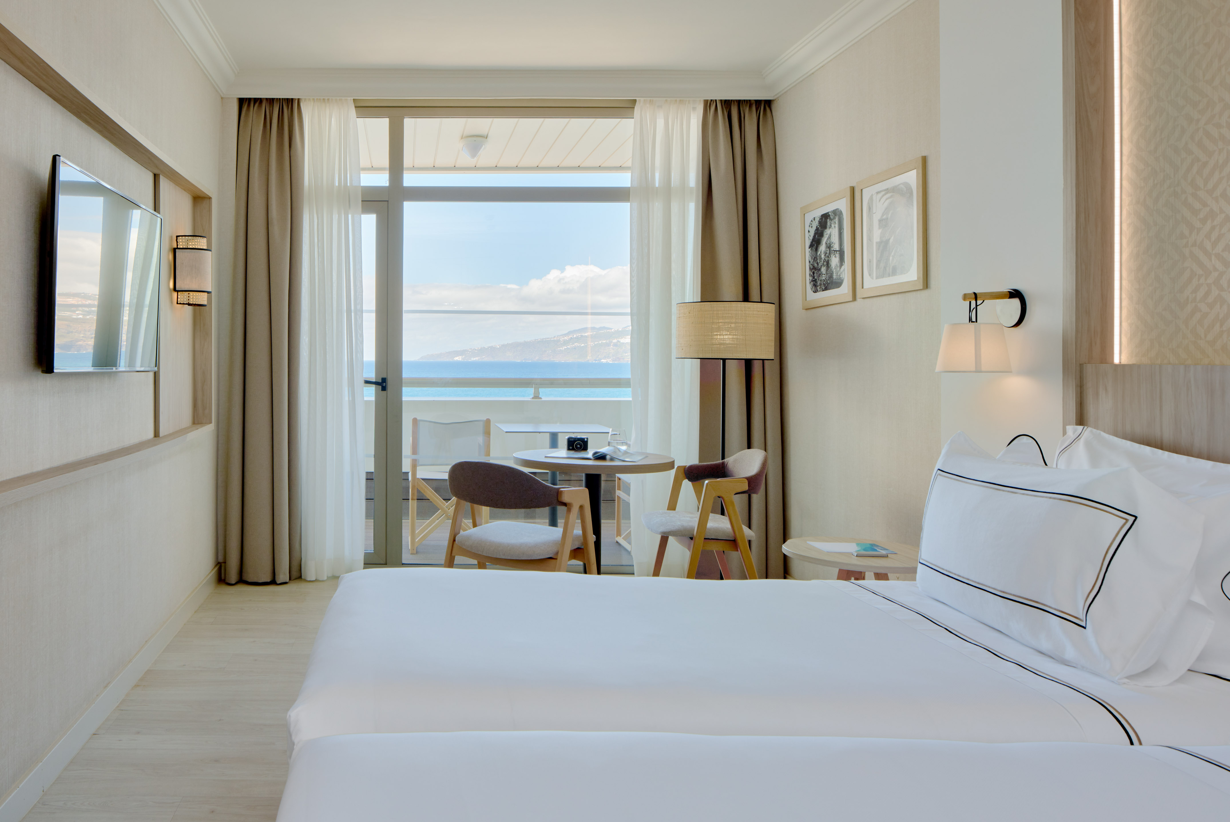 Bright hotel guest room with balcony overlooking the sea and mountains.