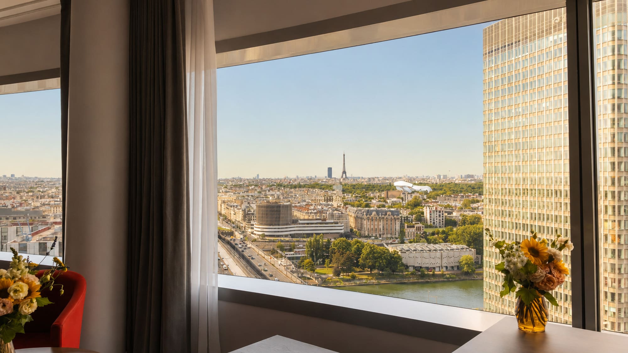 Hotel room window with Paris cityscape, Eiffel Tower, and Seine River view.