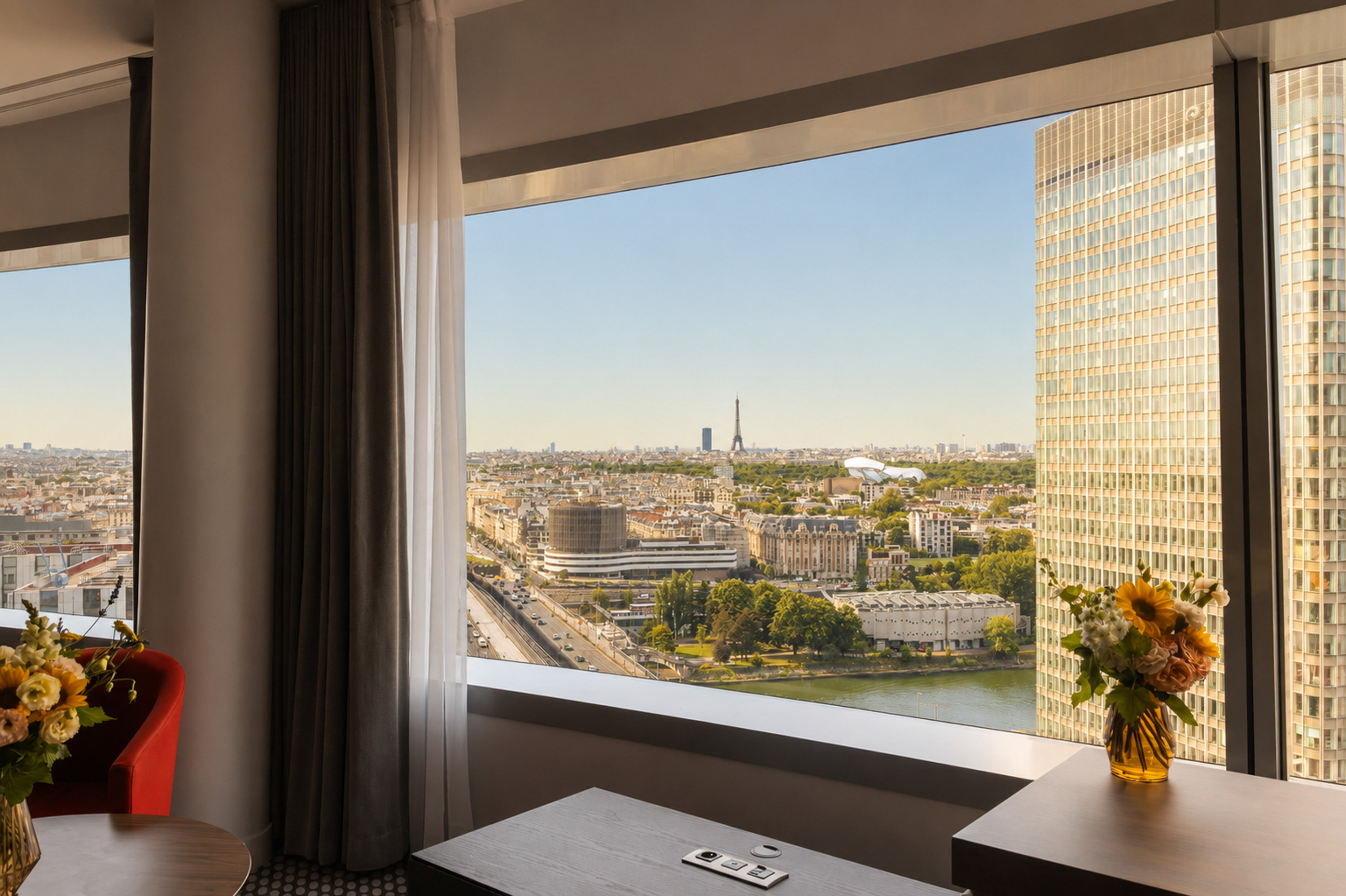 Hotel room window with Paris cityscape, Eiffel Tower, and Seine River view.